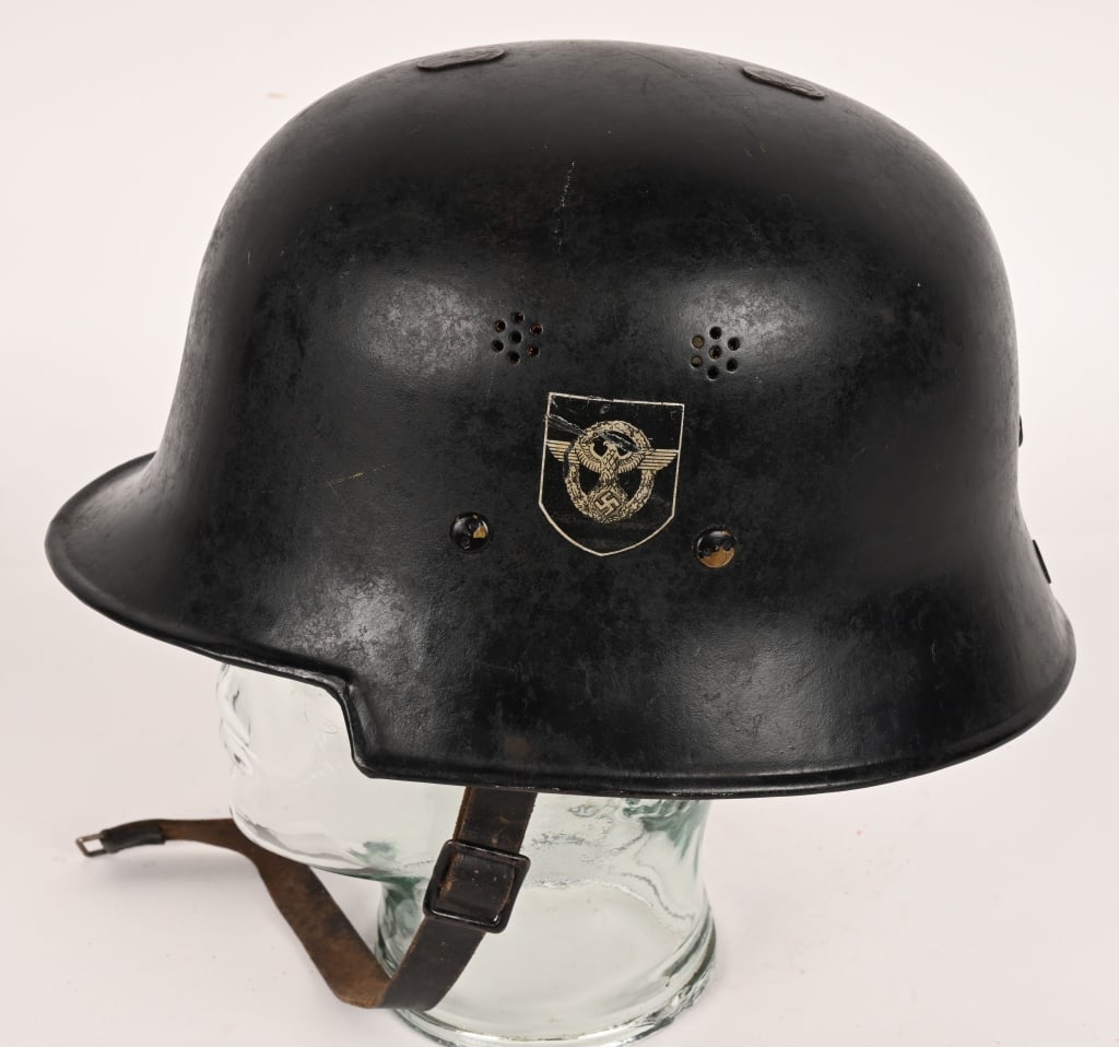 NAZI M34 DOUBLE DECAL FEUERSCHUTZPOLIZEI HELMET: The stamped, sheet steel construction civic M34 helmet retains most of its original black satin finish paint. The left side of the helmet has a silver bordered black based police decal with the second