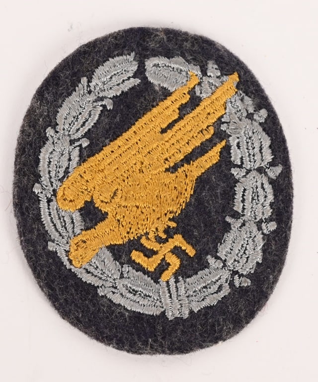 WWII NAZI GERMAN PARATROOPER'S BADGE IN CLOTH: The badge consists of a roughly, 70mm tall, 60mm wide, Luftwaffe blue/gray wool construction, vertically oval, base which features a machine embroidered, stylized "diving" eagle clutching a swastika i
