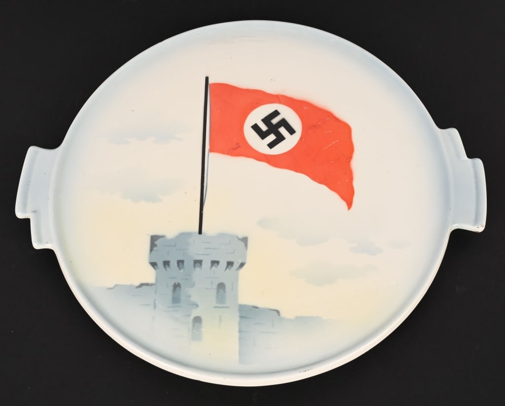 WWII NAZI GERMAN NSDAP PORCELAIN PLATE WITH FLAG: A beautiful Porcelain NSDAP Decorative Plate measuring 14 X 12 1/4 inches depicting a Large NSDAP Banner on top of a Castle. The plate is maker marked to the reverse and in excellent condition. The Na