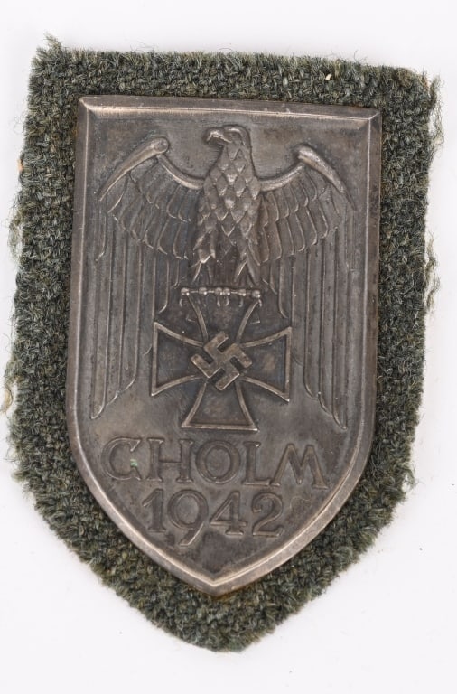 WWII NAZI GERMAN ARMY CHOLM CAMPAIGN SHIELD WW2: In silvered steel sheet (magnetic), with Army cloth backing, in very fine condition. Background and design After the relief of Cholm, a commemorative shield was suggested by General Scherer to&#