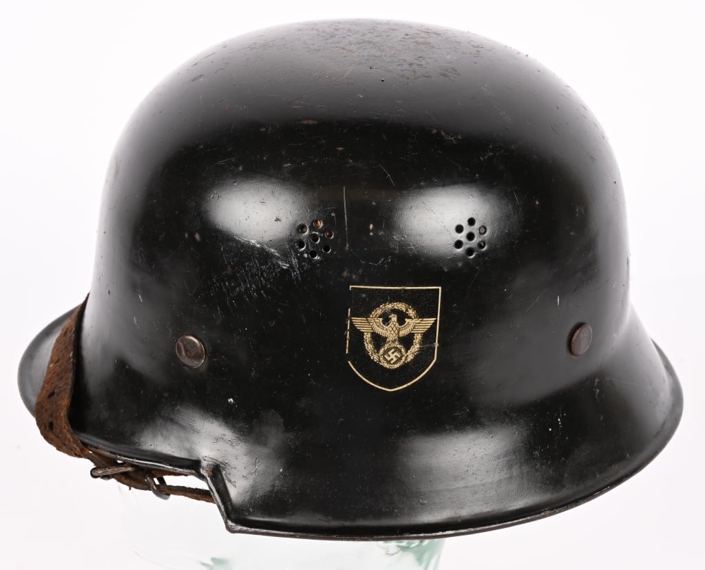 NAZI M34 DOUBLE DECAL FEUERSCHUTZPOLIZEI HELMET: The stamped, sheet steel construction civic M34 helmet retains most of its original black satin finish paint. The left side of the helmet has a silver bordered black based police decal with the second