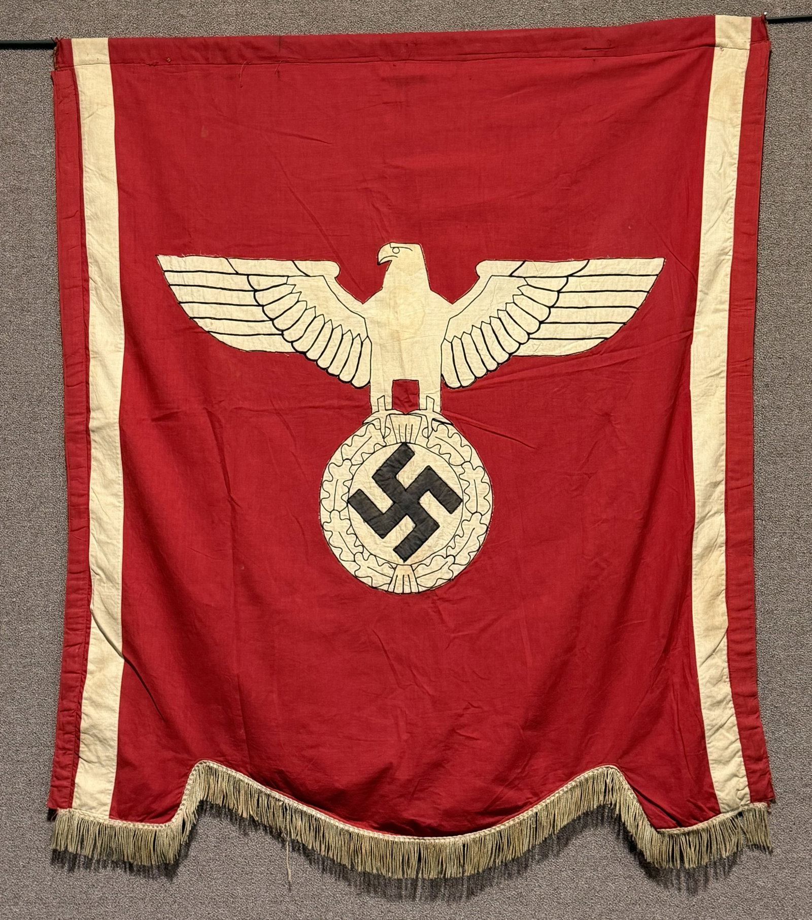 WWII NAZI GERMAN POLITICAL PODIUM BANNER W/ EAGLE: Approximately 55 inches tall, 51 inches wide, single sided, multi-piece, cotton/rayon construction banner features a red base field with a separate early party eagle clutching a canted mobile swastika