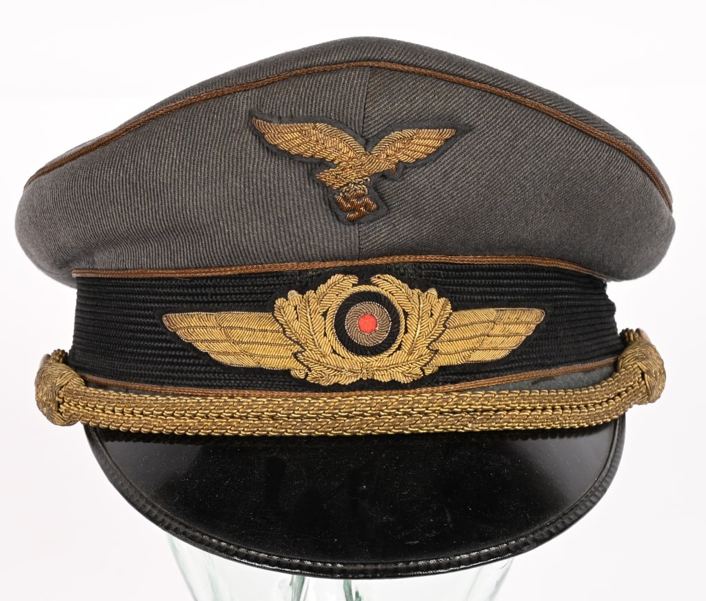 WWII NAZI GERMAN LUFTWAFFE GENERAL’S VISOR CAP: A Luftwaffe Generals visor cap constructed of Luftwaffe-gray cap tricot (Mützen Trikot) with a fine twill weave (Körperbindung) pattern of parallel running ribs. The cap has a traditional hi