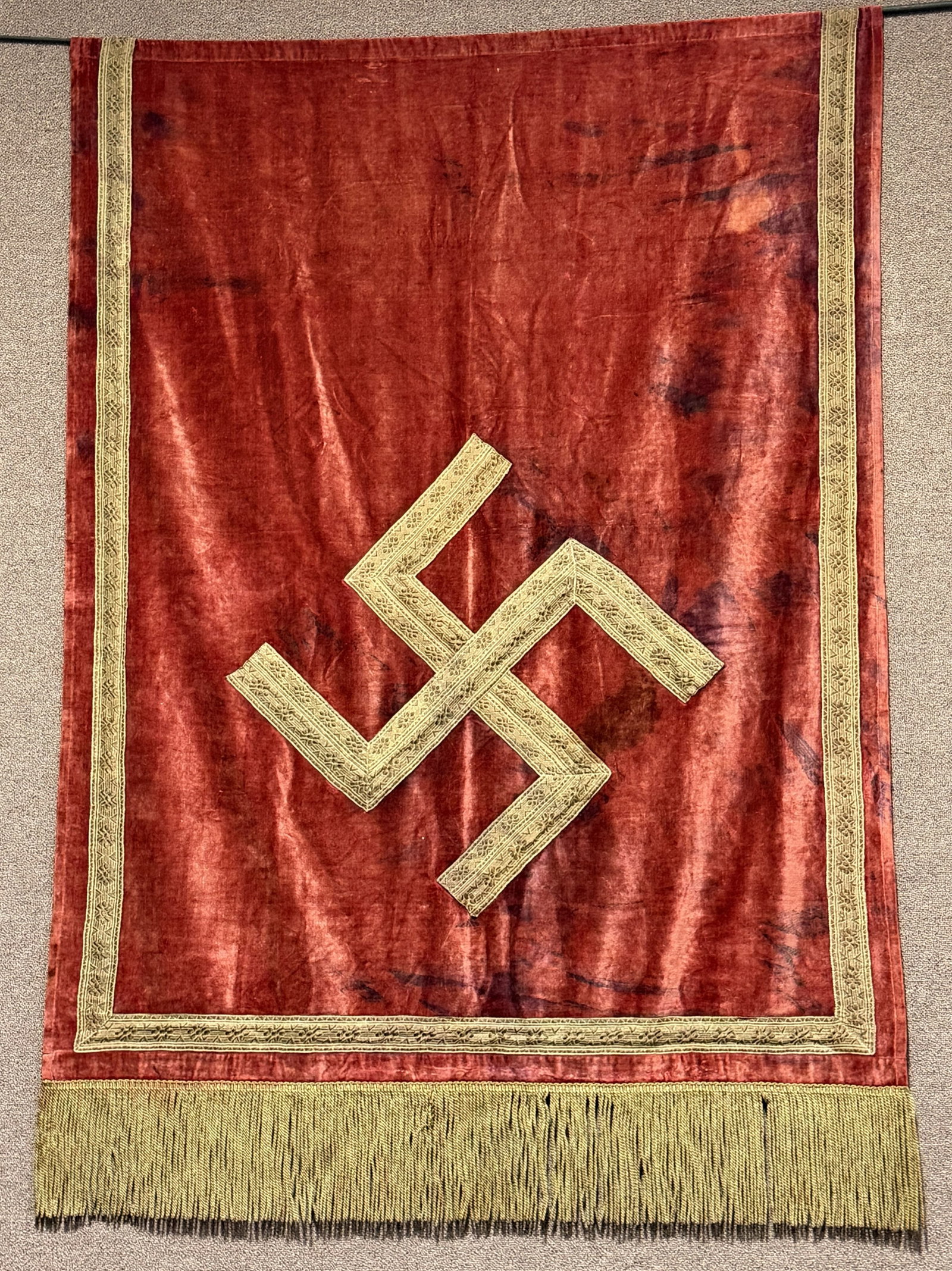 WWII NAZI GERMAN NSDAP POLITICAL PODIUM BANNER WW2: Approximately 62 X 49 inches excluding fringe is single sided multi-piece velvet construction banner features a red base field with a separate gold bullion canted swastika. The bottom edge of the bann