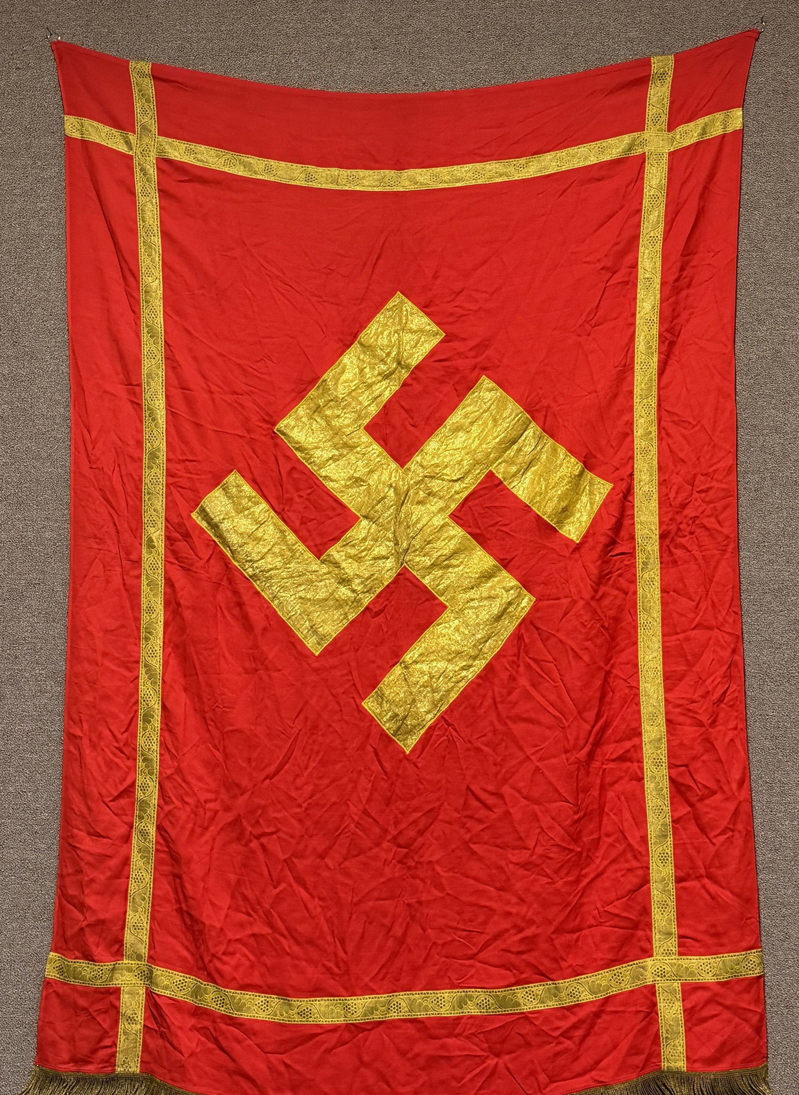 WWII NAZI GERMAN NSDAP POLITICAL PODIUM BANNER WW2: Approximately 68 X 50 inches excluding fringe is single sided multi-piece wool construction banner features a red base field with a separate gold bullion canted swastika. The banner also has a wide go