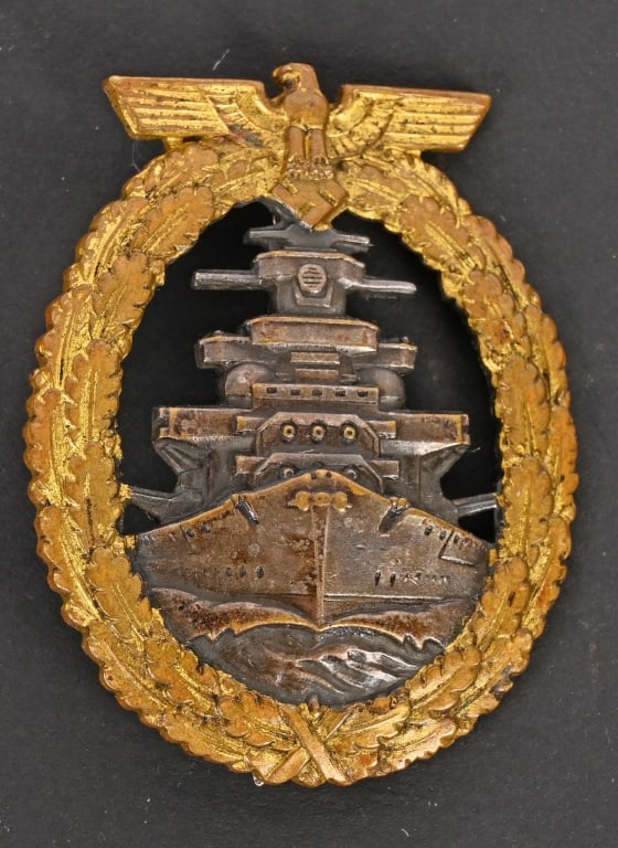 WWII NAZI GERMAN HIGH SEAS FLEET WAR BADGE: Die struck, solid backed, nicely convexed, alloy construction badge with gilt and burnished silver finishes. The badge features a vertically oval oak-leaf wreath with a national eagle with out-stretch