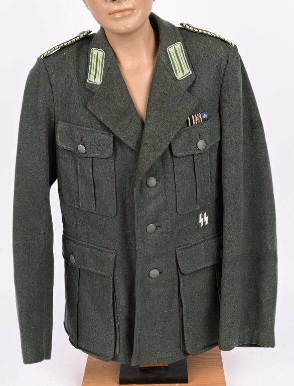 WWII NAZI GERMAN SCHUTZPOLIZEI FORMER SS TUNIC: (Schutzpolizei Feldbluse). A field blouse constructed of green wool featuring a vertical row of three matte-gray pebbled buttons meeting an equal number of reinforced buttonholes The front of the tuni