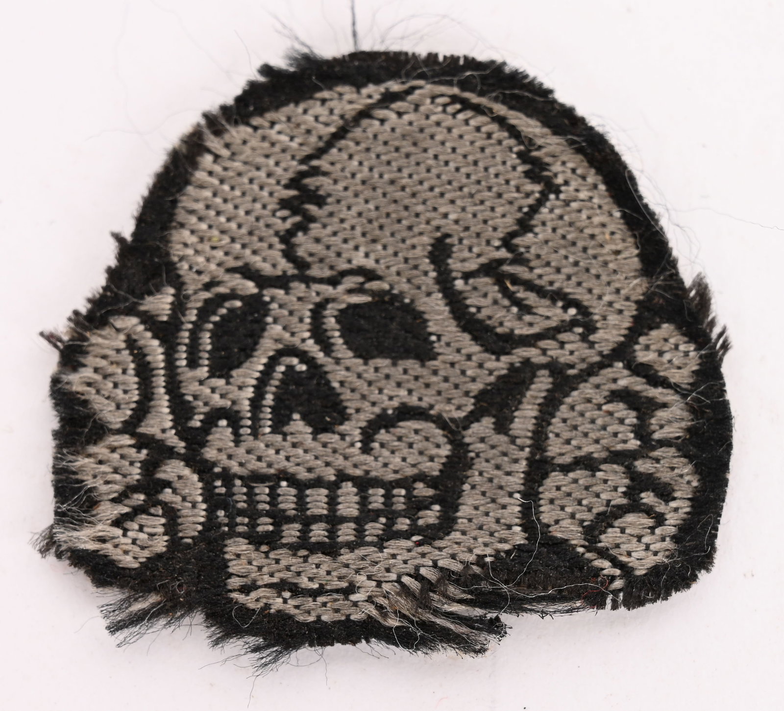 WWII NAZI GERMAN WAFFEN SS M43 OVERSEAS CAP SKULL: BeVo, machine woven construction skull and crossbones in silvery/gray threads with black accent threads on a cut-out woven black rayon base. The skull features a bottom jaw, dual rows of teeth and nic