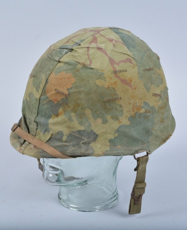 WW2 M1 Helmet with Camo Cover, Named: Helmet is pre 1944 with front seam and swivel bales. Has cloth camo cover. Liner is marked Firestone, and parts of lining may have been replaced for re-issue. Inside of rim of helmet marked Elsmore. V