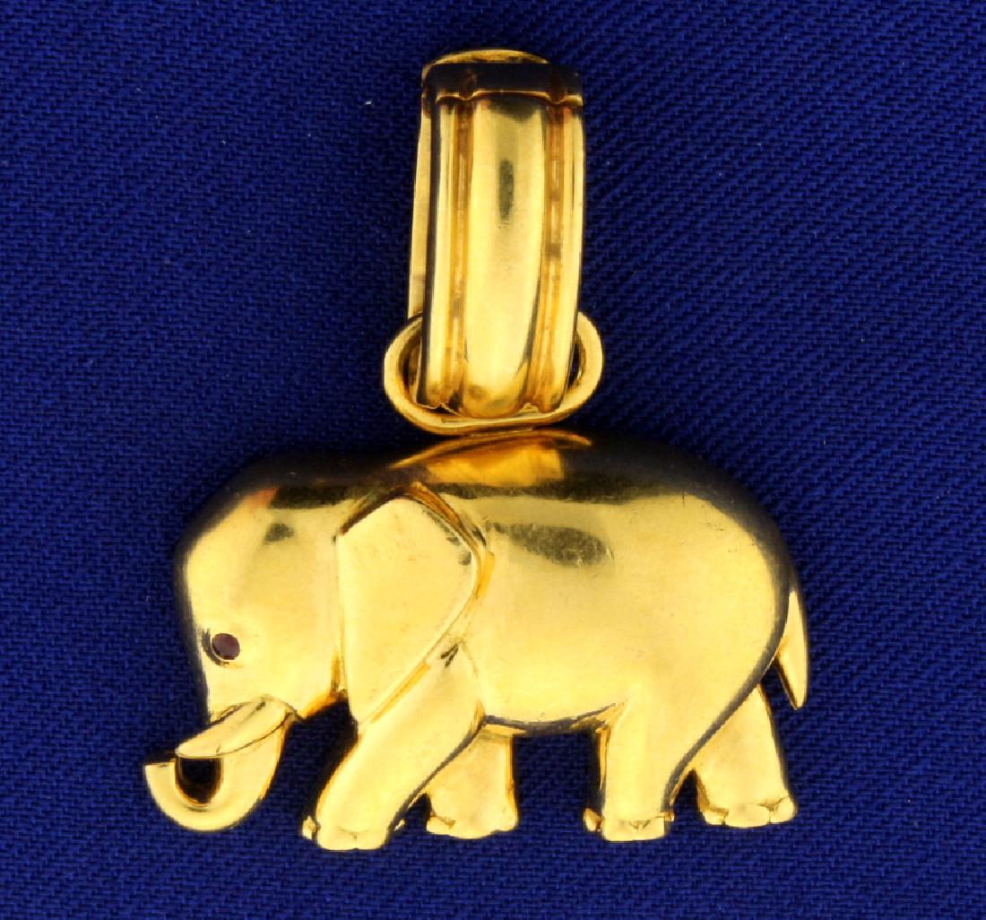 18k Elephant Pendant: In 18k yellow gold. The elephant has a 1.25mm ruby as an eye. 1 1/2 inches long with bale that can open to accommodate up to a 12mm chain or omega. 1 1/4 inch wide. 15.5g.