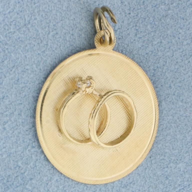 Marriage or Wedding Anniversary Charm in 14k Yellow Gold: 14k yellow gold. 1 Inch long (including jump ring) by 3/4 Inch wide. Florentine finish with engagement ring and wedding band 3D design. Contains one CZ gemstone in engagement ring. 1.7g.