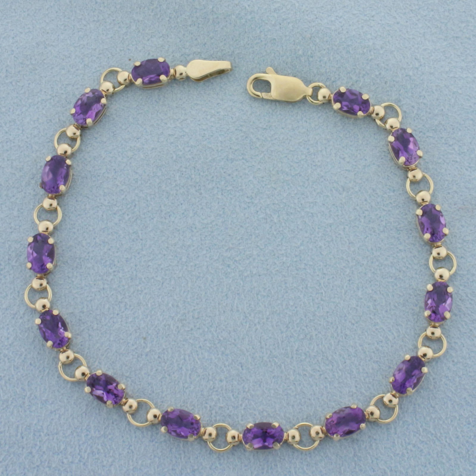 Amethyst Tennis Line Bracelet in 10k Yellow Gold: In 10k yellow gold. Contains 14 high quality natural 6mmx4mm oval cut Amethyst gemstones with excellent color and clarity. Approximately 7ct TW. Lobster clasp. 7 1/4 inches long. 5.2g.