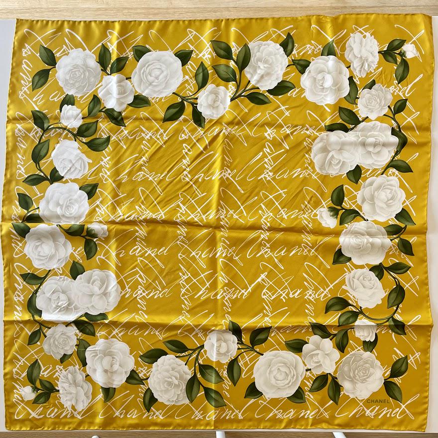 Chanel Vintage Camellia Flower Script Signature Silk 90 Scarf: Guaranteed authentic with box. Measures approx. 33" x 34" (90cm), 100% silk, and hand rolled edges. Bold yellow gold, green, white, and off-white colorway. Flowers surrond the repeated script Chanel s