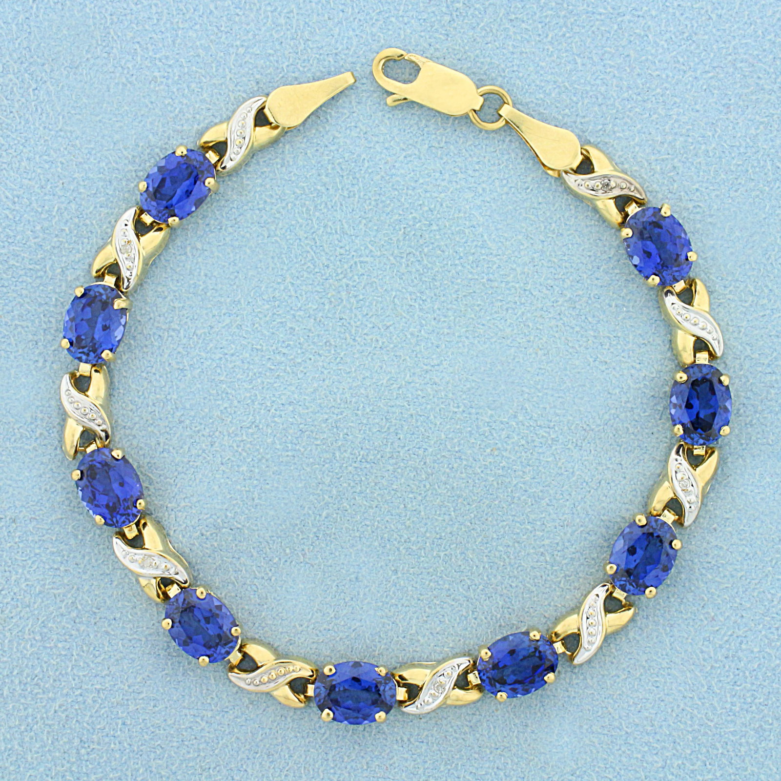 13ct TW Lab Sapphire and Diamond Line Bracelet in 10K Yellow and White Gold: In 10K Yellow and White Gold. Contains nine high quality 8 x 6mm oval cut Lab Sapphire gemstones with vibrant blue color and excellent clarity. Also contains five high quality 1/2pt Diamonds. 7 1/4 in