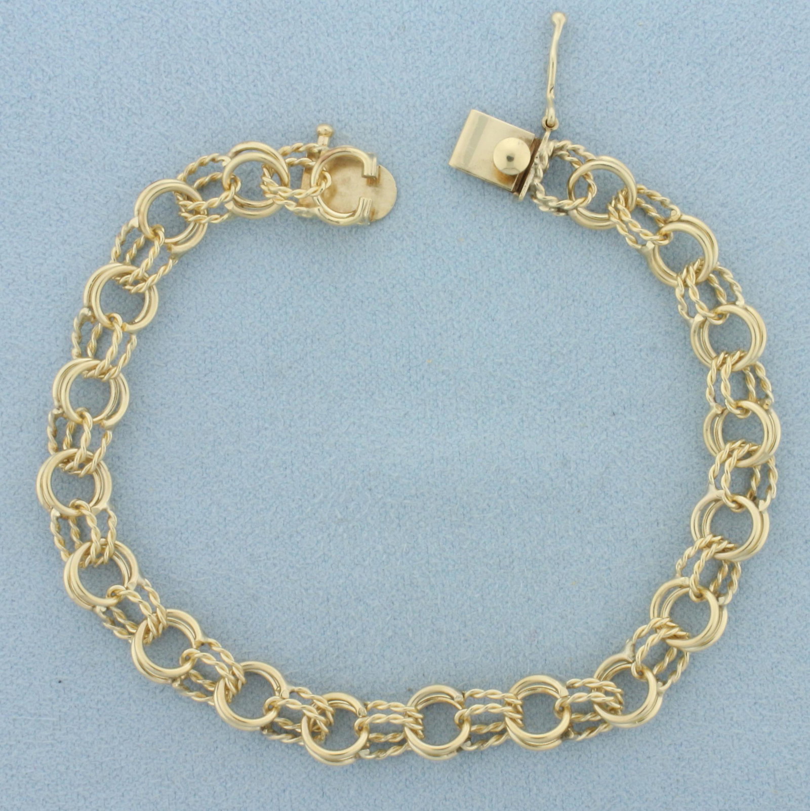 Double Ring Charm Bracelet in 14k Yellow Gold: In 14k yellow gold. 7 1/4 inches long x 8mm wide. Concealed slide clasp with safety latch. Unique alternating smooth and braided design double links. 11.1g.
