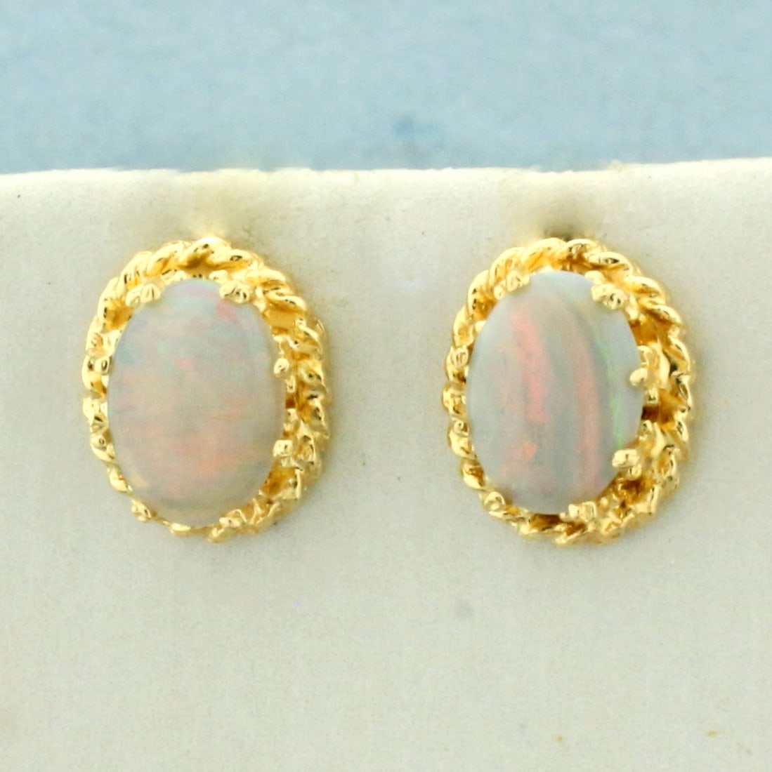 Opal Stud Earrings in 14k Yellow Gold: In 14k yellow gold. Contains 2 high quality natural 7mm by 5mm oval gemstones with vibrant color of play with flashes of green, blue, orange, and red. Friction backs. 1.4g.