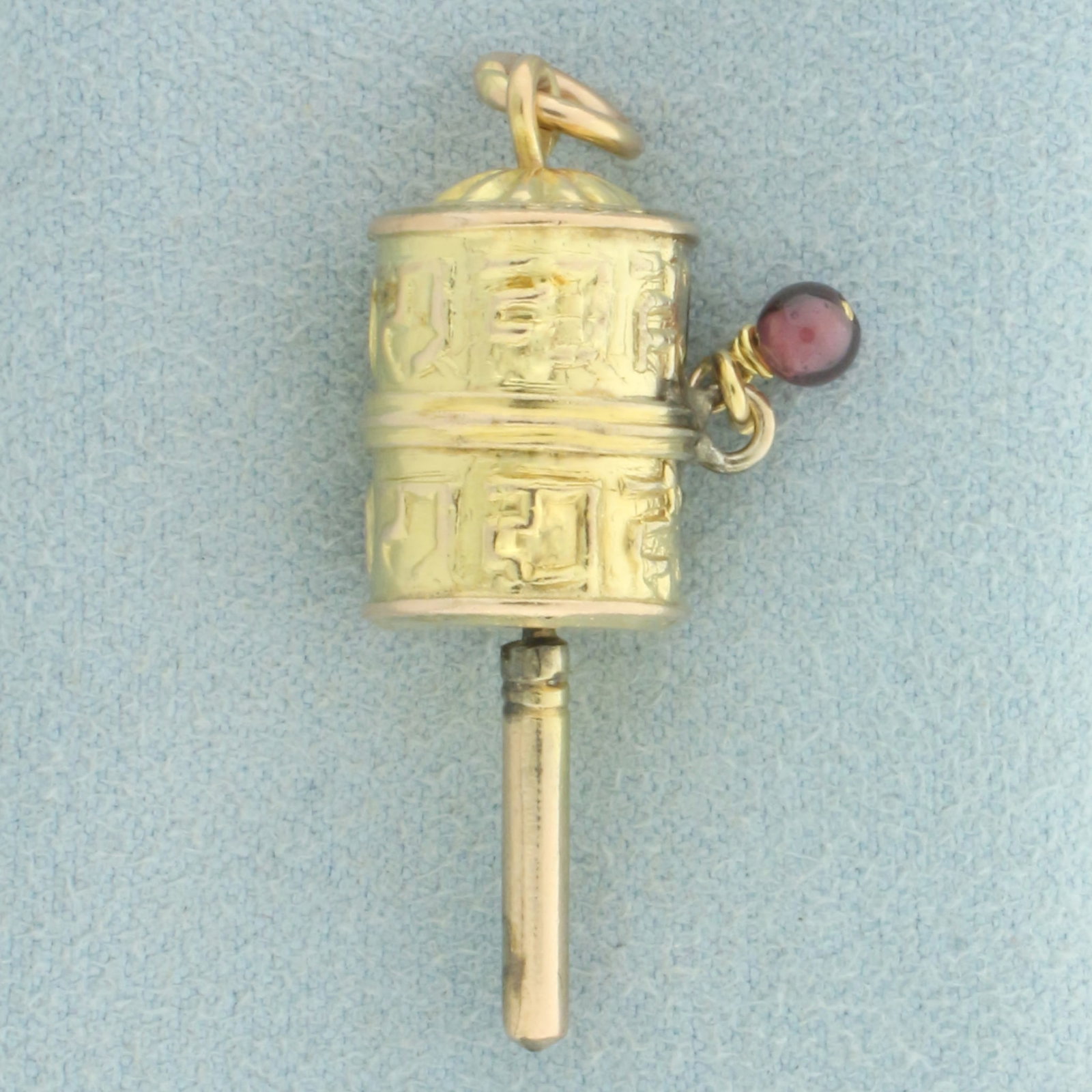 Mechanical Tibetan Buddhist Prayer Wheel Pendant or Charm in 14k Yellow Gold: In 14k yellow gold. Contains one high quality natural 3.5mm Ruby gemstone bead with vibrant color. 1 3/8 inches long and 1/2 inches wide. Wheel spins. 2.3g.