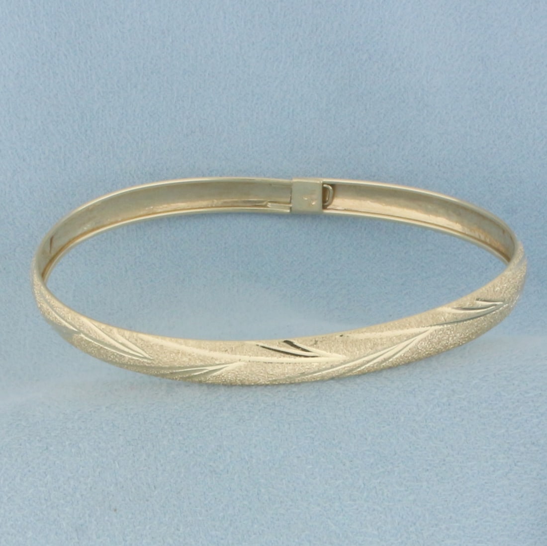 Sandblast Finish Leaf Design Bangle Bracelet in 10k Yellow Gold: In 10k yellow gold. Interior dimensions: 2.5 inches x 2 1/8 inches. 6.1mm wide. Sandblast finish with leaf nature design. Opens/closes with safety latch for easy putting on/taking off. 4.3g.