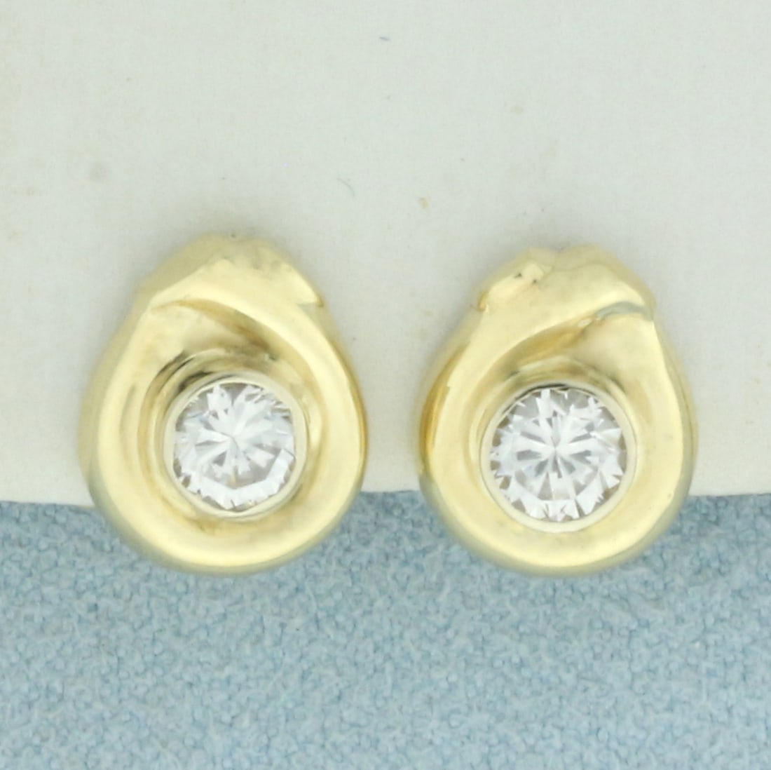 Bezel Set CZ Earrings in 18k Yellow Gold: In 18k yellow gold. Contains two high quality CZ gemstones, 3/4ct TW, with excellent cut and clarity for added brilliance. 3/8 inches long and 3/8 inches wide. Omega backs. 4.6g.