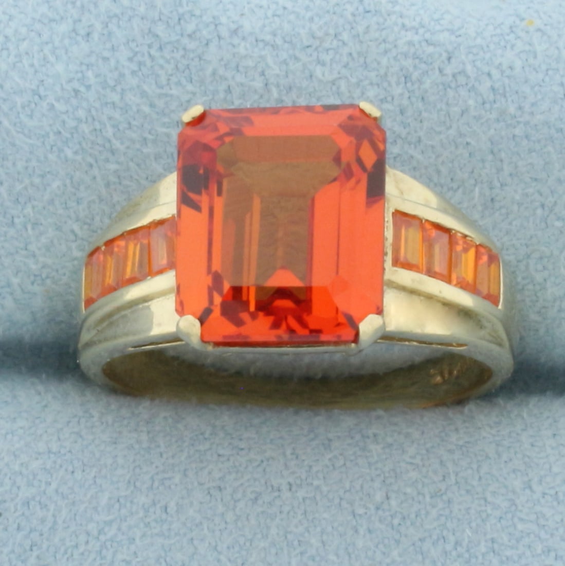 Lab Orange Sapphire Ring in 10k Yellow Gold: In 10k yellow gold. Contains one 12mm x 10mm and 8 2.8mm x 2.3mm emerald cut lab sapphire gemstones with intense orange color and excellent clarity. Size 10. 6.1g.