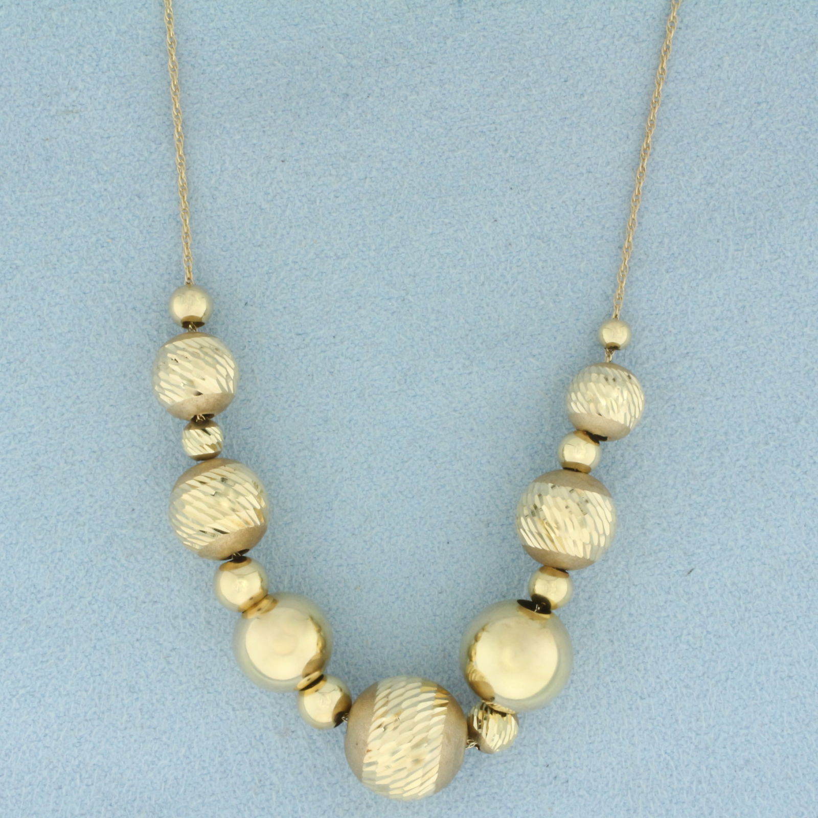 Diamond Cut Ball Bead Necklace in 14k Yellow Gold: In 14k Yellow Gold. 24 inches long. Largest bead is 11mm diameter. Ball beads are diamond cut for added brilliance. Chain is .95mm thick. Unique push clasp. 4.8g.