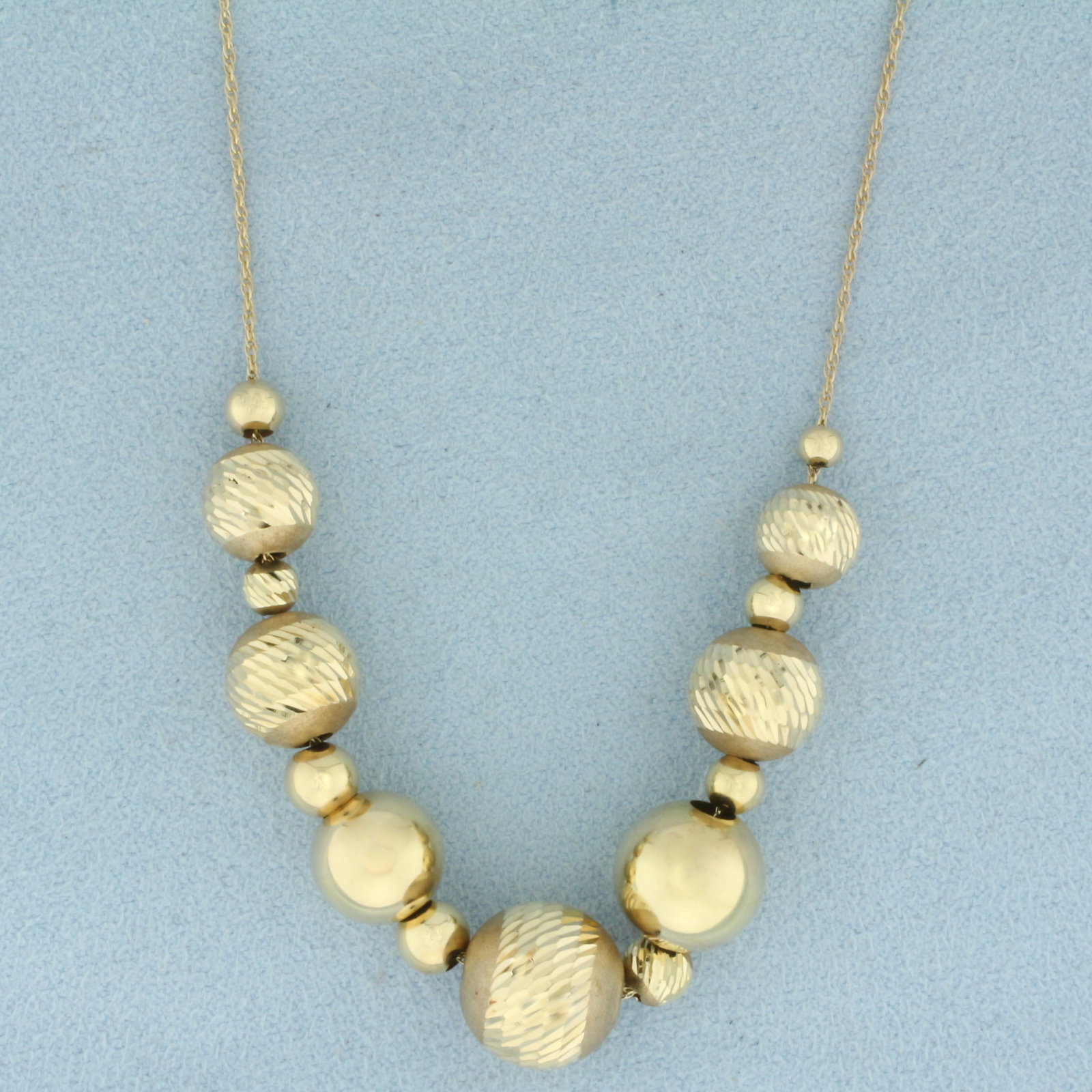 Diamond Cut Ball Bead Necklace in 14k Yellow Gold: In 14k Yellow Gold. 24 inches long. Largest bead is 11mm diameter. Ball beads are diamond cut for added brilliance. Chain is .95mm thick. Unique push clasp. 4.8g.