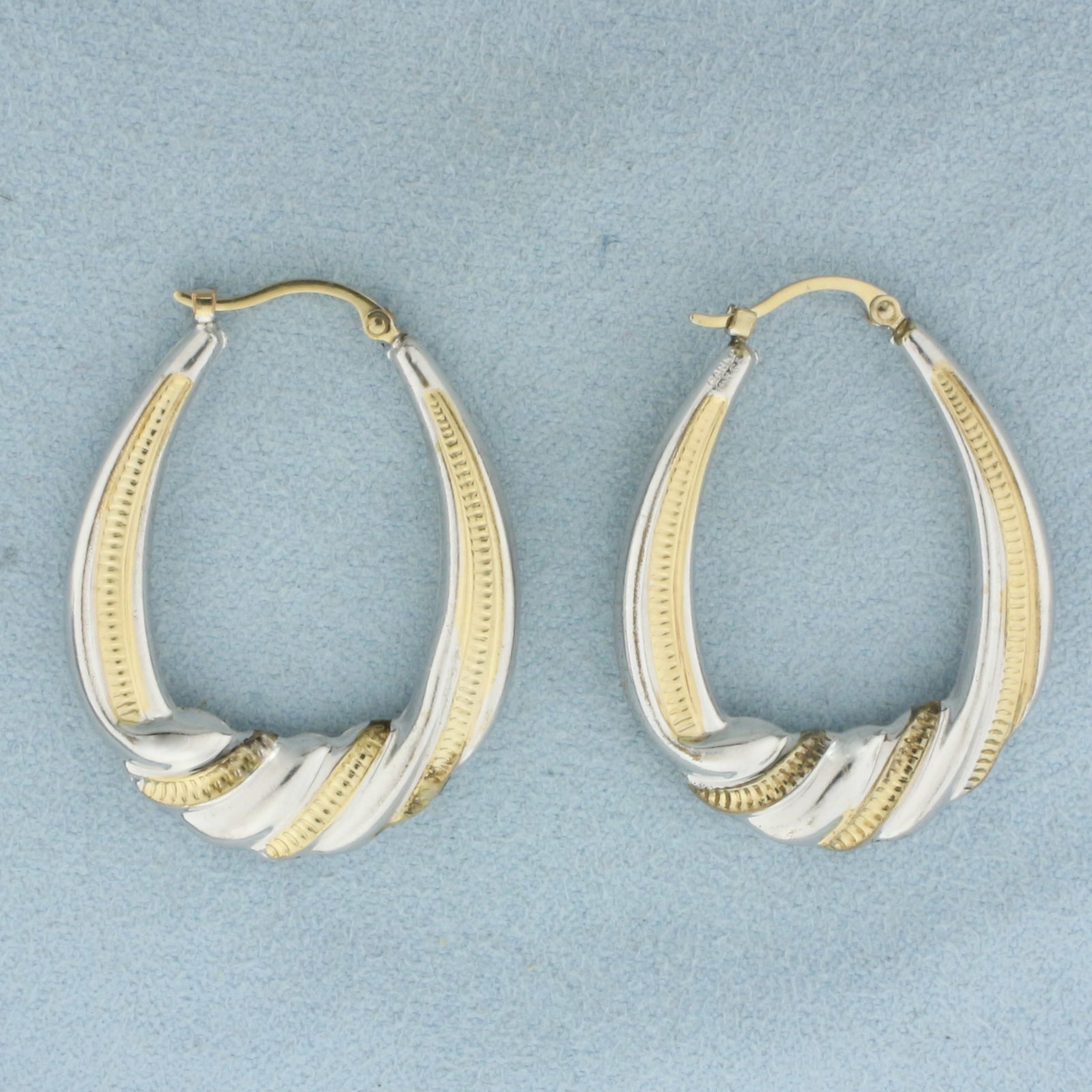 Twisting Two Tone Hoop Earrings in 14k Yellow and White Gold: In 14k Yellow and White Gold. 1 1/4 inch long. 1 inch wide. Hinged backs. 2.7g.