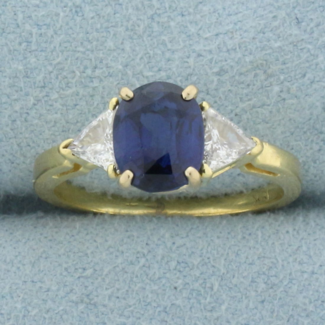 AAA Sapphire and Trillion Diamond Ring in 18k Yellow Gold: In 18k yellow gold. Contains one high quality natural AAA quality oval cut sapphire, 7.8mm x 6.3mm, approximately 1.75cts, with intense royal blue color and excellent clarity. Also contains two high q