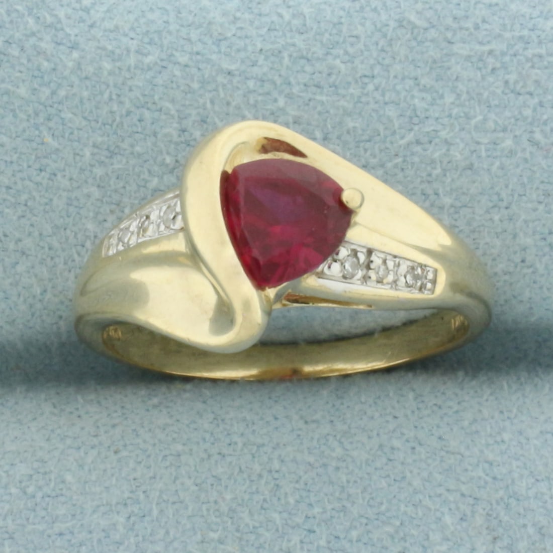 Trillion Ruby and Diamond Ring in 10k Yellow Gold: In 10k Yellow Gold. Contains one 6mm high quality trillion Ruby gemstone, with vivid color and excellent clarity. Also contains six high quality diamonds, .05ct TW. 10.6mm wide at center. Size 8. 3.4g