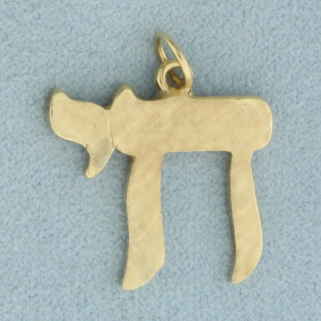 Hebrew Chai Pendant or Charm in 14k Yellow Gold: In 14k Yellow Gold. 7/8 inch long including bail. 3/4 inch wide. Unique textured finish. Chai in Hebrew means "To Life" and is a symbol of health and vitality. 3.2g.