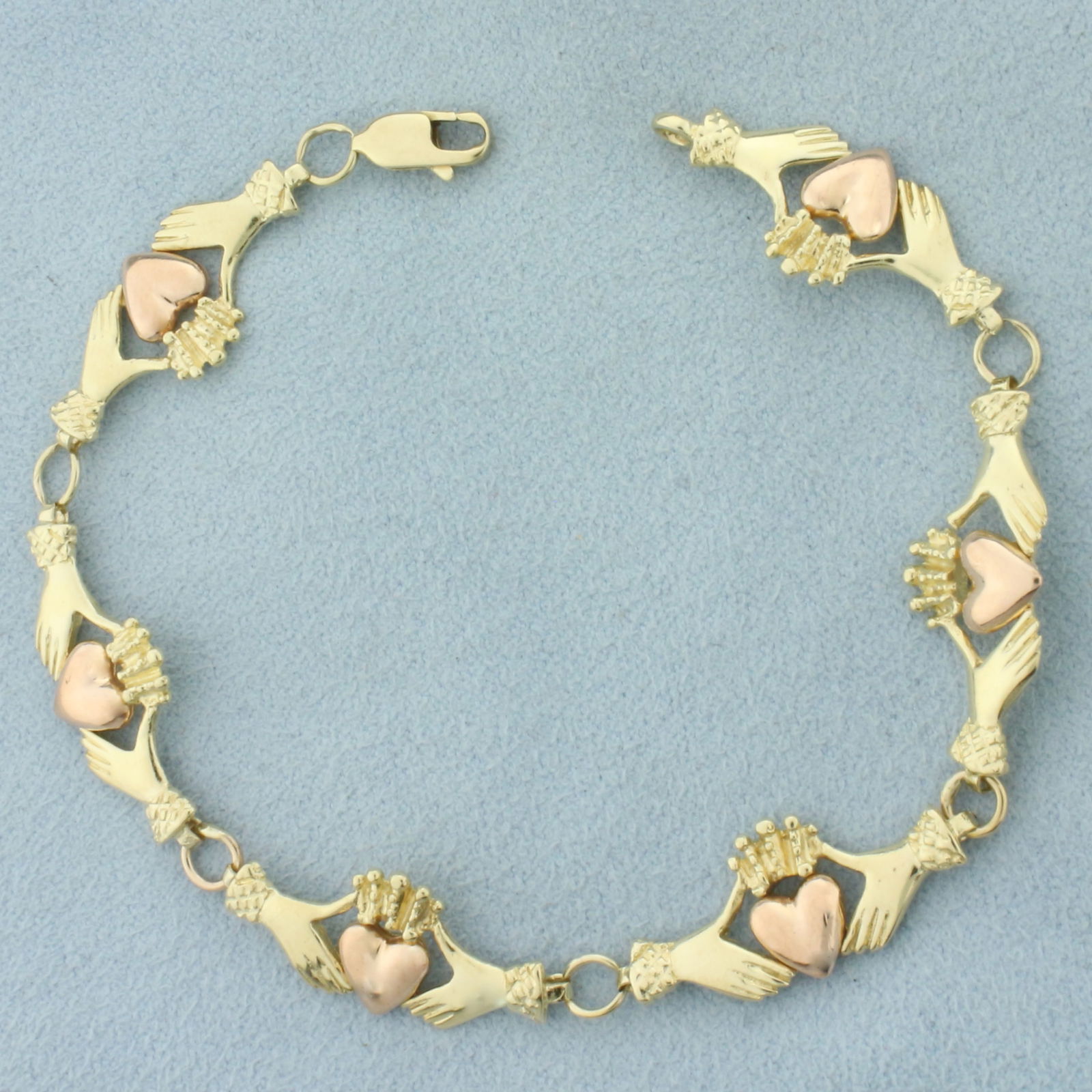 Claddagh Bracelet in 14k Yellow and Rose Gold: In 14k Yellow and Rose Gold. 7 1/4 inches long. 3/8 inch wide. Lobster clasp. 8.6g