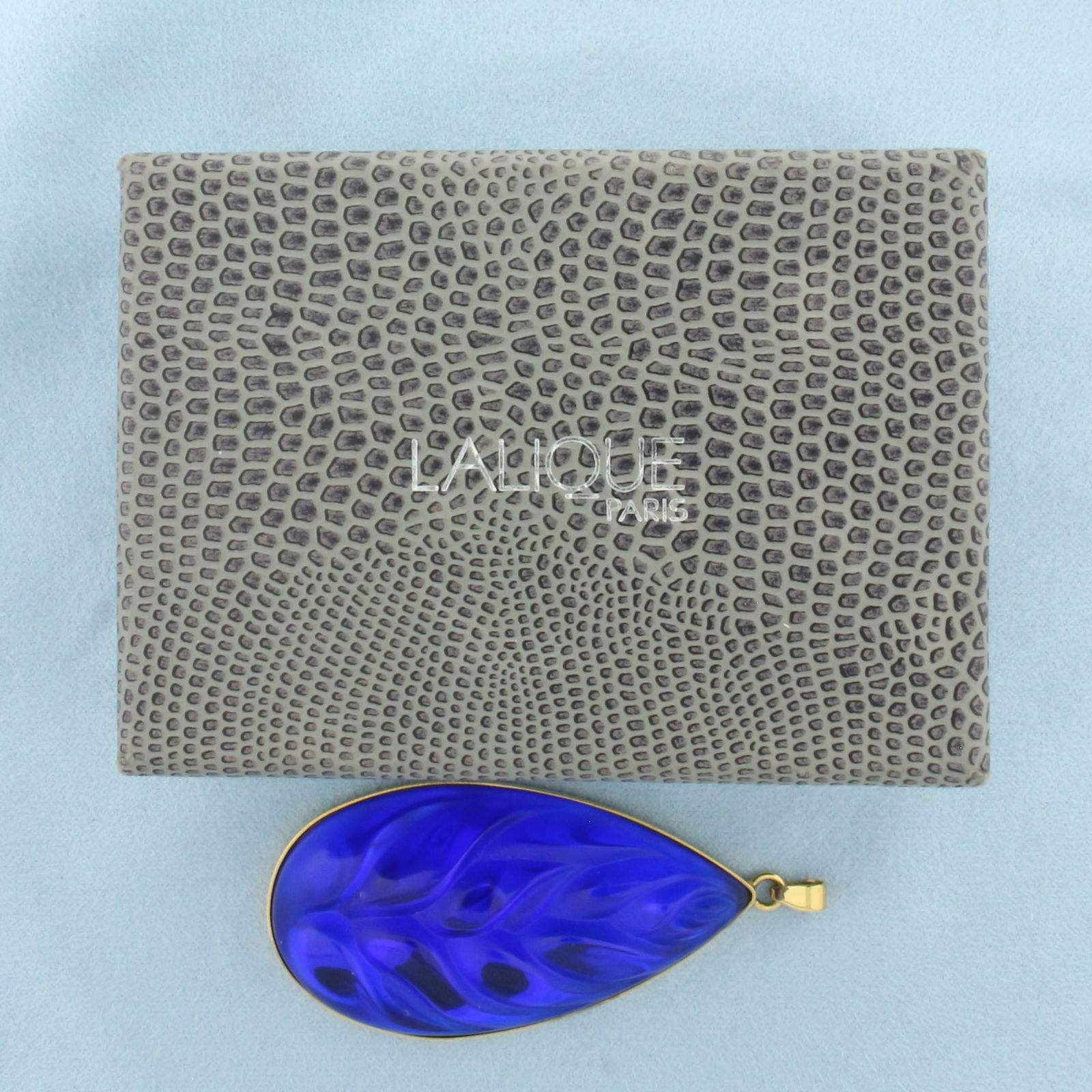 Lalique Crystal Blue Heliconia Leaf Pendant: Gold plated. Marked "Lalique France" on back. 2.5" x 1-1/8". Box included.