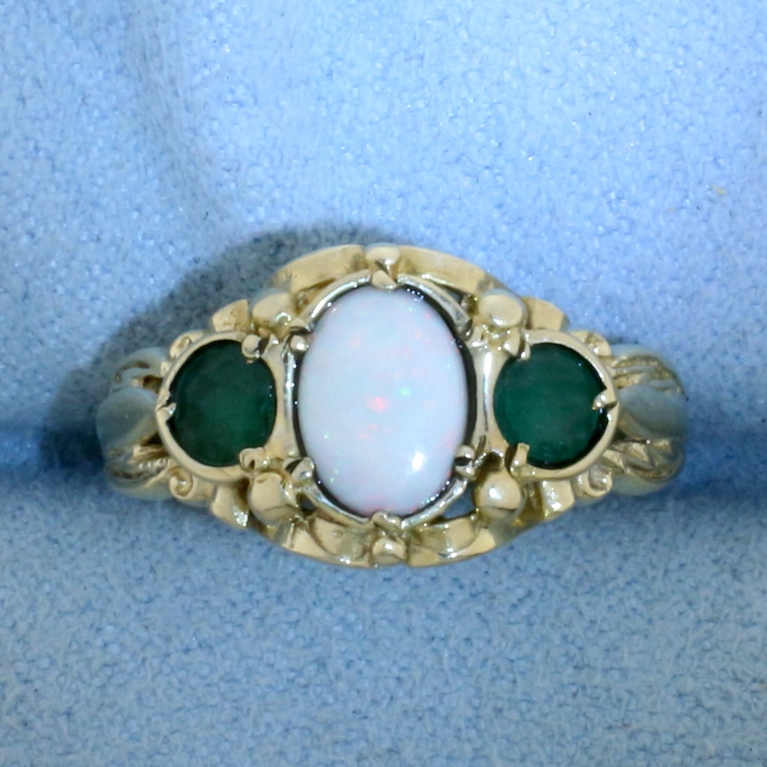 Vintage Opal and Emerald Ring in 9k Yellow Gold: In 9k Yellow Gold. Contains one 7.5x5mm high quality natural Opal gemstone with flashes of pink, orange, blue and green. Also contains two 4mm high quality natural Emerald gemstones with intense color