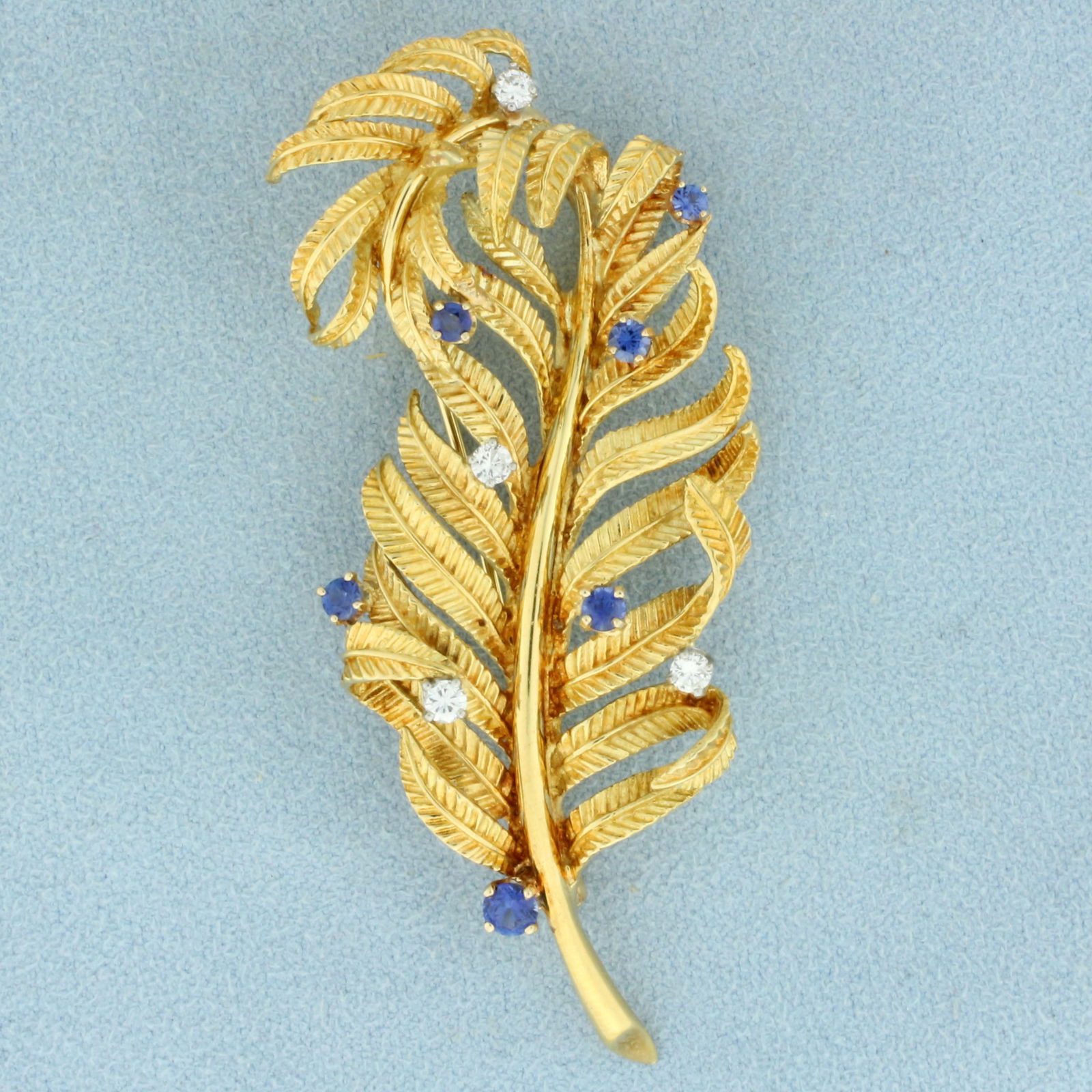 Vintage Sapphire and Diamond Feather Brooch in 18K Yellow Gold: In 18K Yellow Gold. Contains six AAA quality Sapphire gemstones ranging from 2.5mm to 3.5mm each with vibrant blue color and excellent clarity. Also contains four high quality 0.06ct Diamonds, VS clar