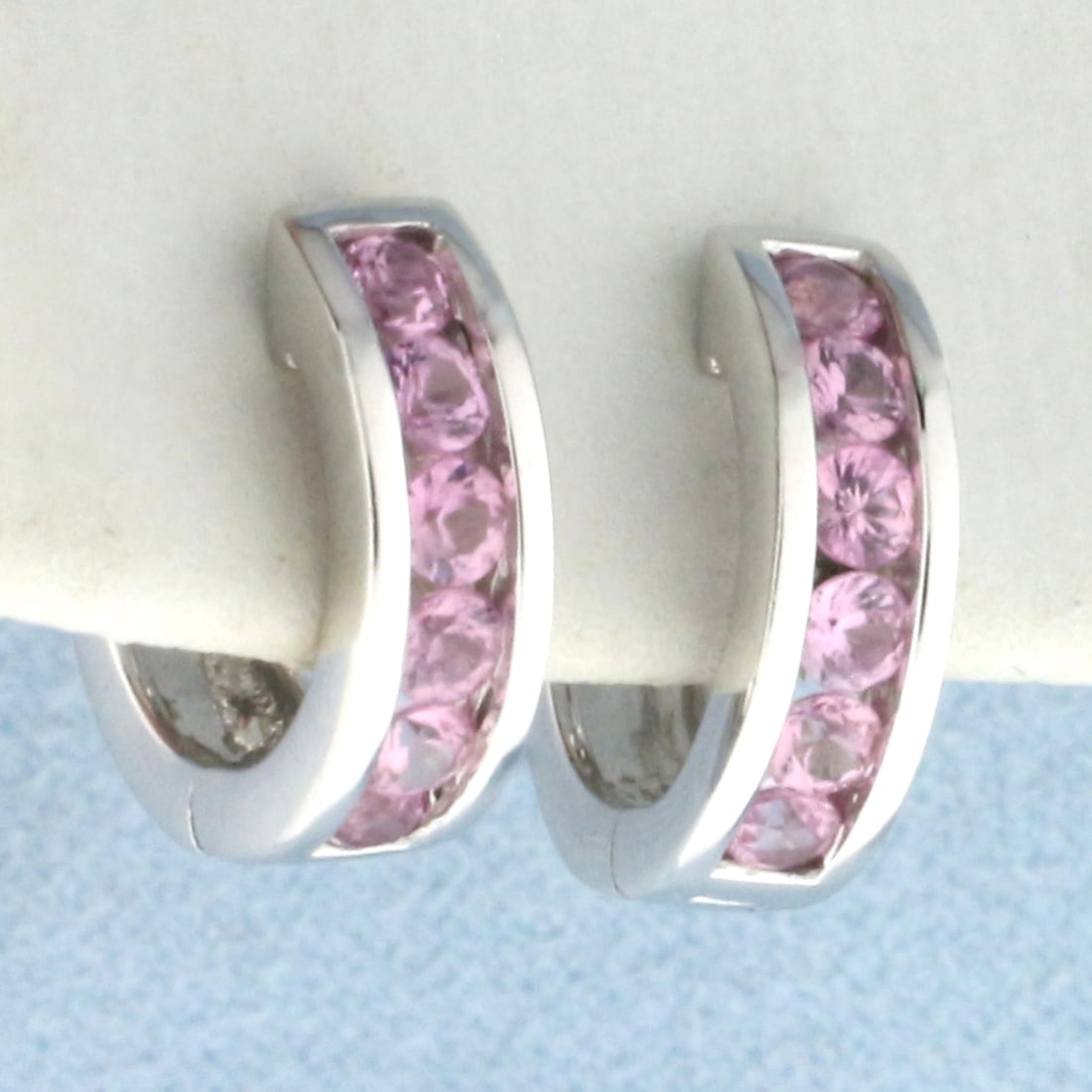 Pink Sapphire Huggie Hoop Earrings in 14k White Gold: In 14k white gold. Contains twelve high quality natural 2.5mm Pink Sapphire gemstones with vibrant color and excellent clarity. 1/2 inch diameter, 4mm wide. Hinged locking closure. 3.6g.
