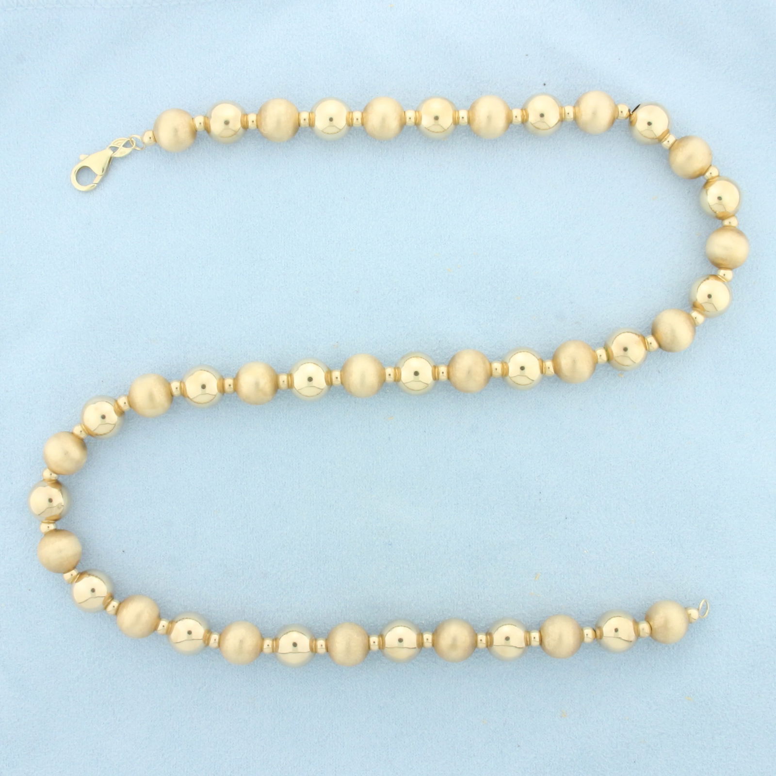 20 Inch Gold Ball Bead Necklace in 14k Yellow Gold: In 14k Yellow Gold. 20 inches long. 10mm beads. Alternating satin and high polish finish gold ball beads for unique look. Lobster clasp. 17.4g.