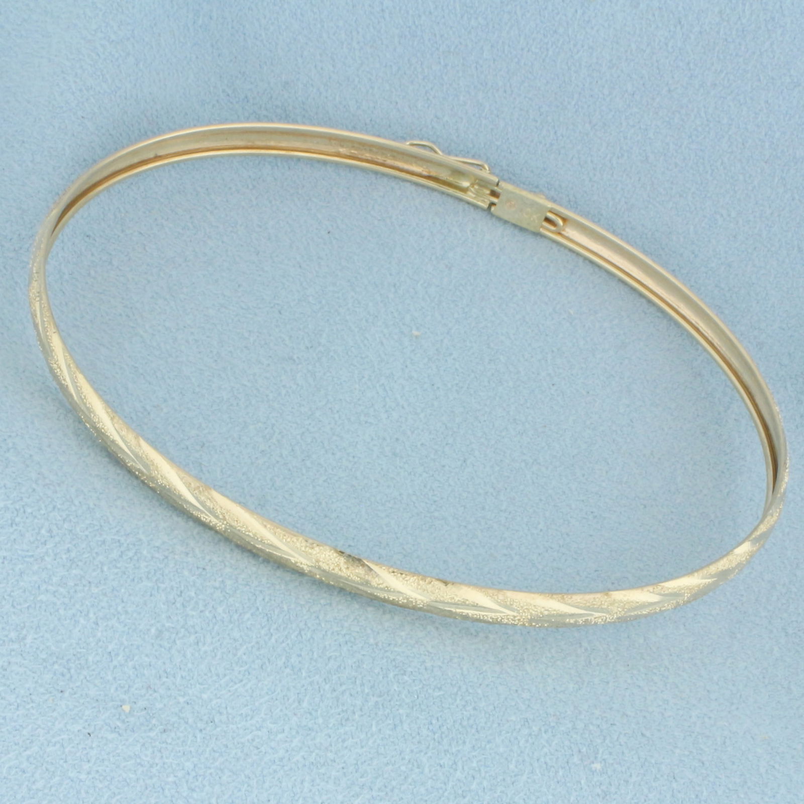 Sandblast Finish Bangle Bracelet in 10k Yellow Gold: In 10k Yellow Gold. Interior dimensions: 2 7/8 inch by 2 1/4 inch. 5mm wide. Sandblast and diamond cut finish. Concealed clasp with safety latch. 3.4g.