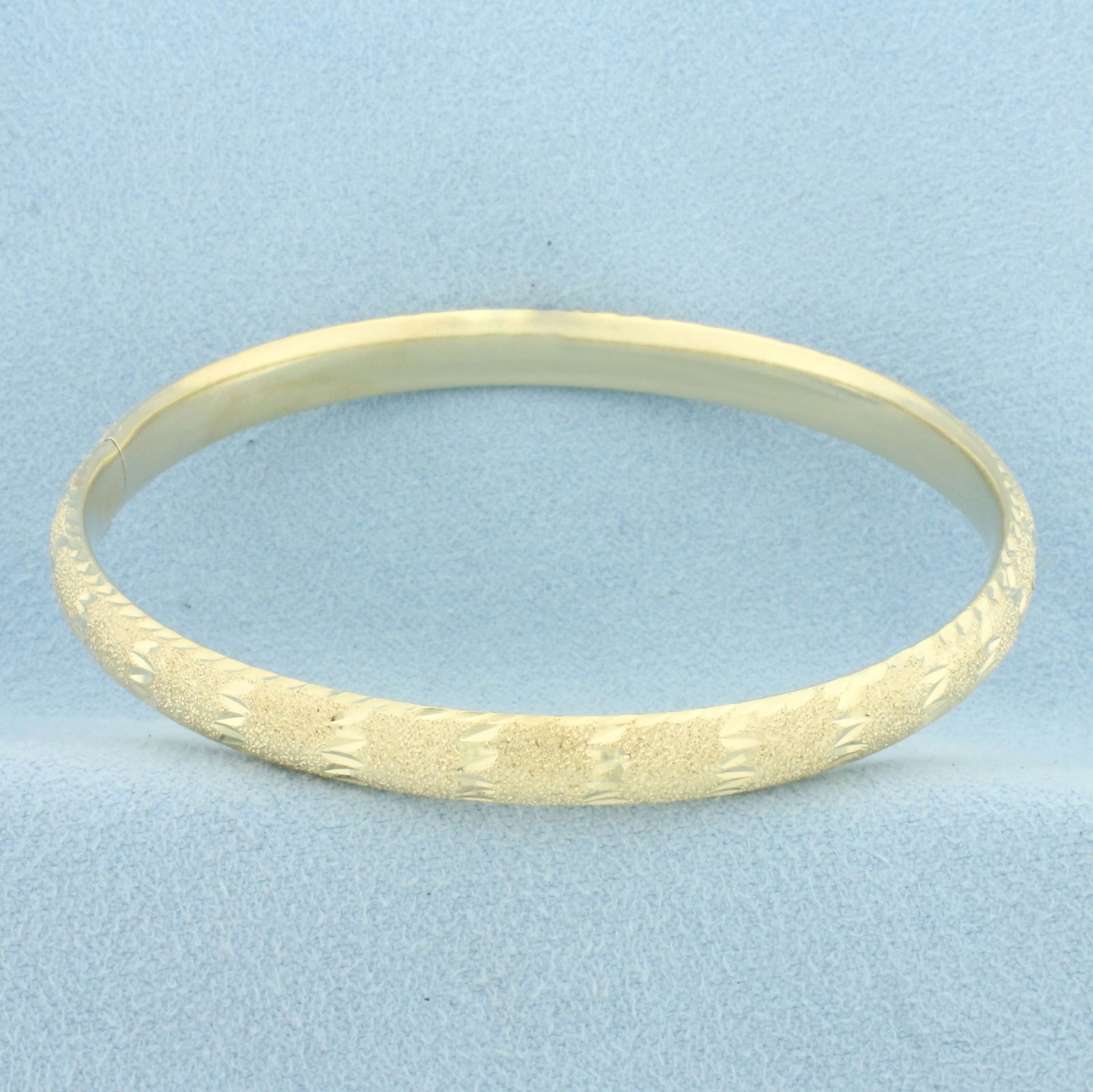 Sandblast and Diamond Cut Finish Hinged Bangle Bracelet in 14k Yellow Gold: In 14k Yellow Gold. Interior dimensions: 2 3/8 inch x 2 1/4 inch. 6.2mm wide. Hinged design with locking slide clasp. 8.1g.