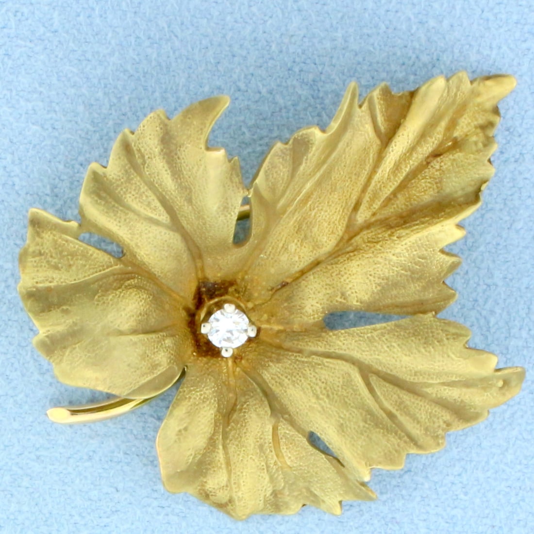 Numbered Designer Diamond Maple Leaf Brooch in 14k Yellow Gold: In 14k yellow gold. Textured matte finish. 1 5/8 inches by 1 3/8 inches. Contains one .1ct round brilliant diamond, VS clarity/H color. Numbered "1648W". 6.8g.