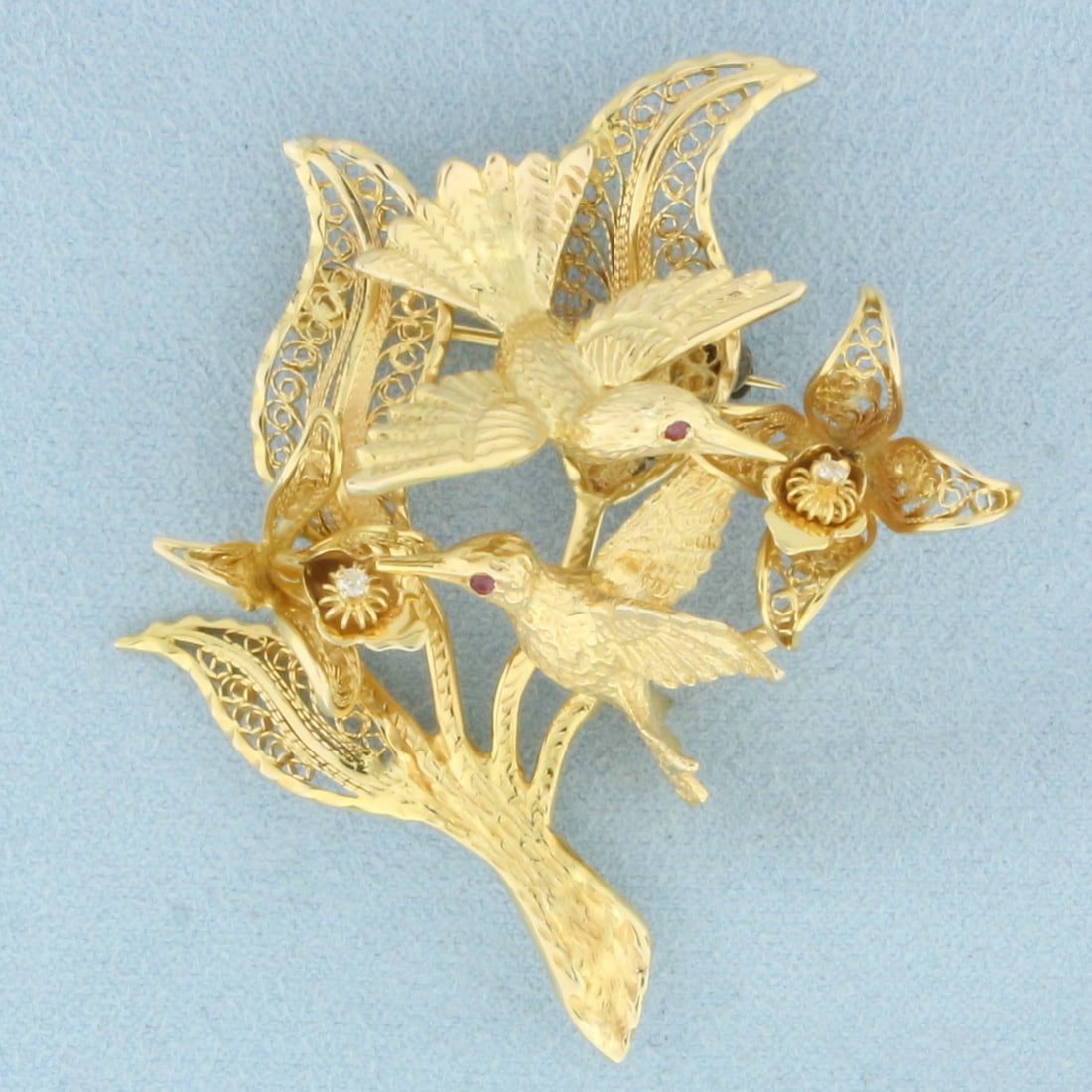 Hummingbirds and Flowers Ruby and Diamond Brooch in 14k Yellow Gold: In 14k Yellow Gold. Contains two 1.4mm high quality natural Ruby gemstones with intense color. Also contains two .02ct high quality diamonds, VS clarity/F color. 2 1/4 inches long. 1 3/4 inch wide. 21
