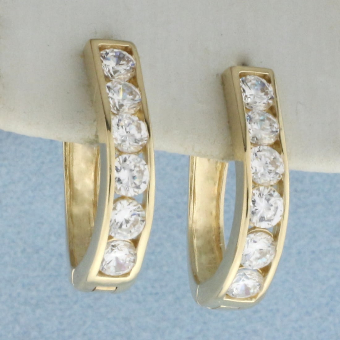 Channel Set CZ Hinged Hoop Earrings in 14k Yellow Gold: In 14k yellow gold. Contains twelve high quality CZ gemstones, 1ct TW, with excellent cut and clarity for added brilliance. 5/8 inches long and 5/8 inches high. Hinged locking closure. 3.6g.