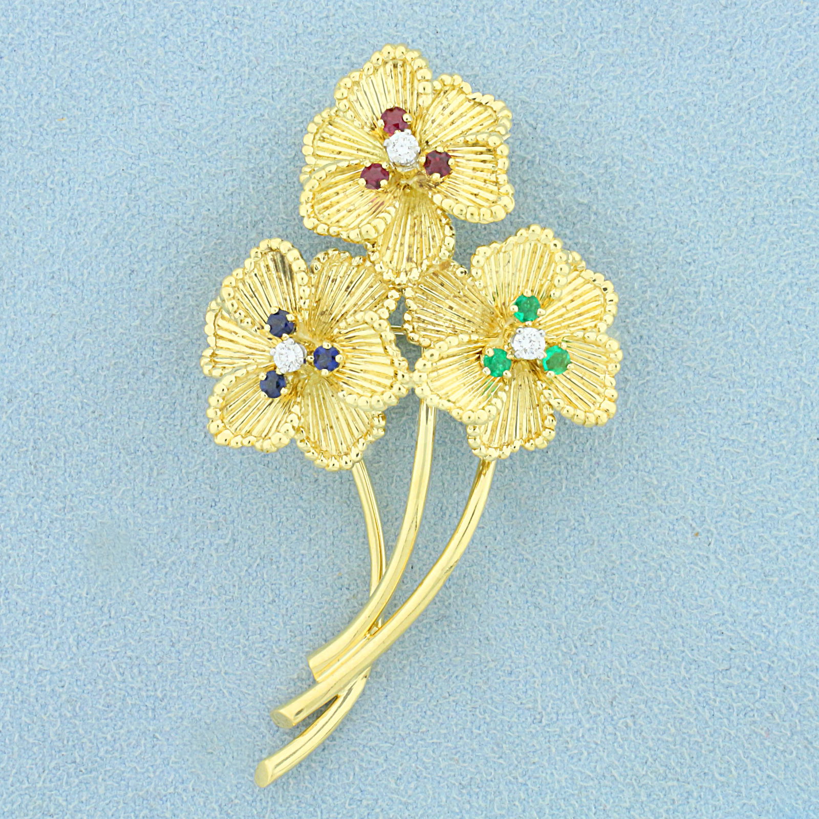 Designer Dankner Flower Pin with Emerald, Sapphire, Ruby, and Diamond in 18K Yellow Gold: In 18K Yellow Gold. Contains three Emerald, three Sapphire and three Ruby high quality natural 2.5mm gemstones, all with vibrant color and excellent clarity. Also contains three high quality .05ct rou