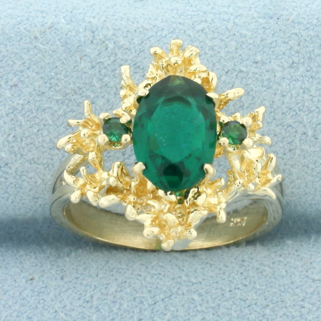 Lab Emerald Designer Ring in 14k Yellow Gold: In 14k Yellow Gold. Contains one 10mmx7mm oval and two 2mm round lab Emerald gemstones, with vibrant color and excellent clarity. 18.6mm wide at center of ring. Size 7.25. 7.1g.