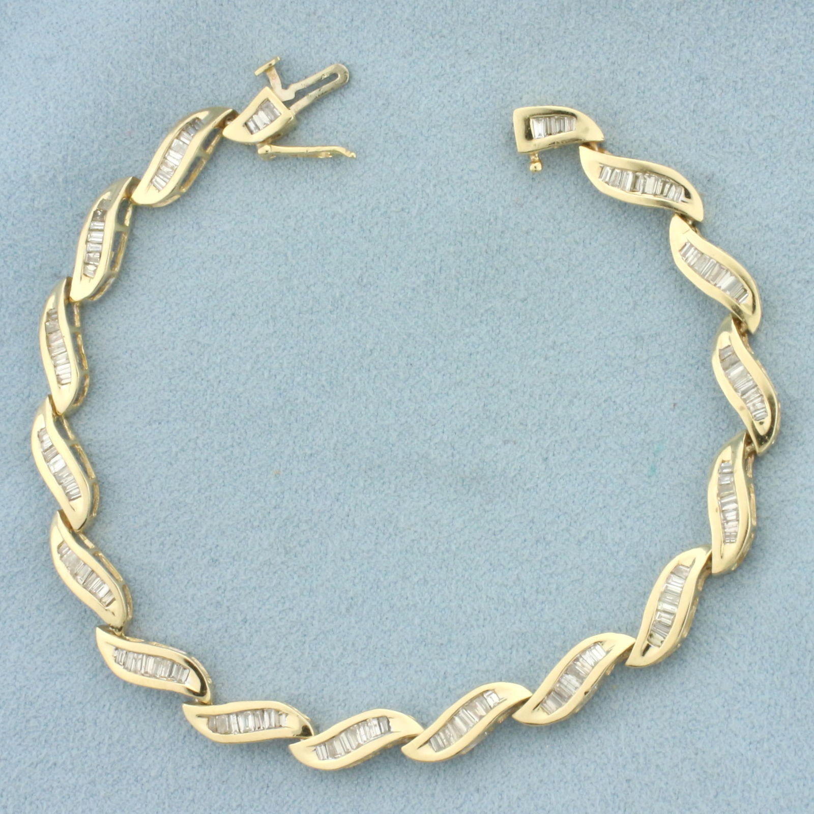 Baguette Diamond Wave Design Tennis Bracelet in 14k Yellow Gold: In 14k Yellow Gold. Contains one hundred and twenty-six high quality baguette diamonds, 2ct TW, SI clarity/G color. 7 1/4 inches long. 1/4 inch wide. Concealed slide clasp with safety latch. 11.1g.