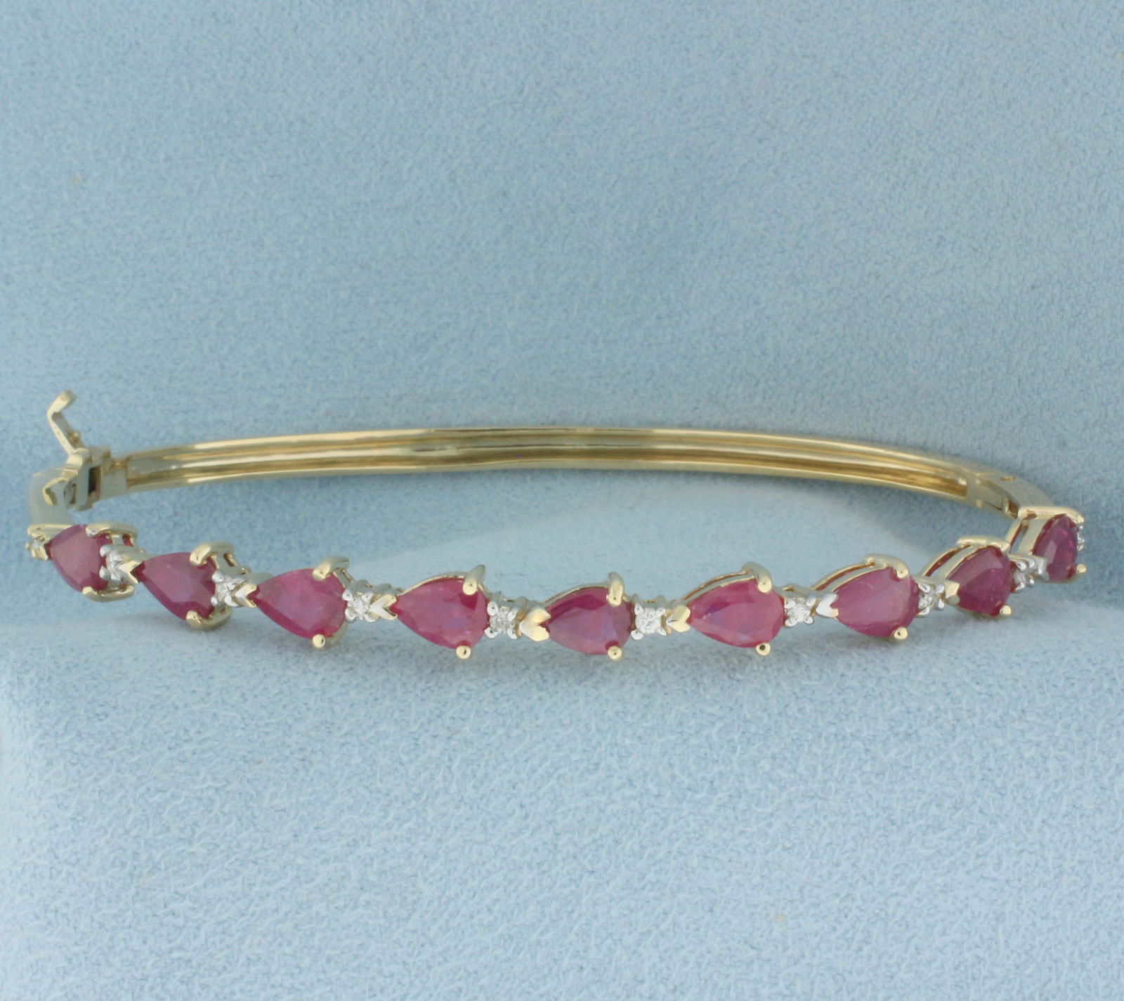 Ruby and Diamond Hinged Bangle Bracelet in 14k Yellow Gold: In 14k yellow gold. Contains 9 high quality natural 6mmx4mm pear shaped ruby gemstones with vibrant color. Also contains ten .01ct high quality diamonds, SI clarity/H color. 2 1/2 inch by 1 7/8 inch
