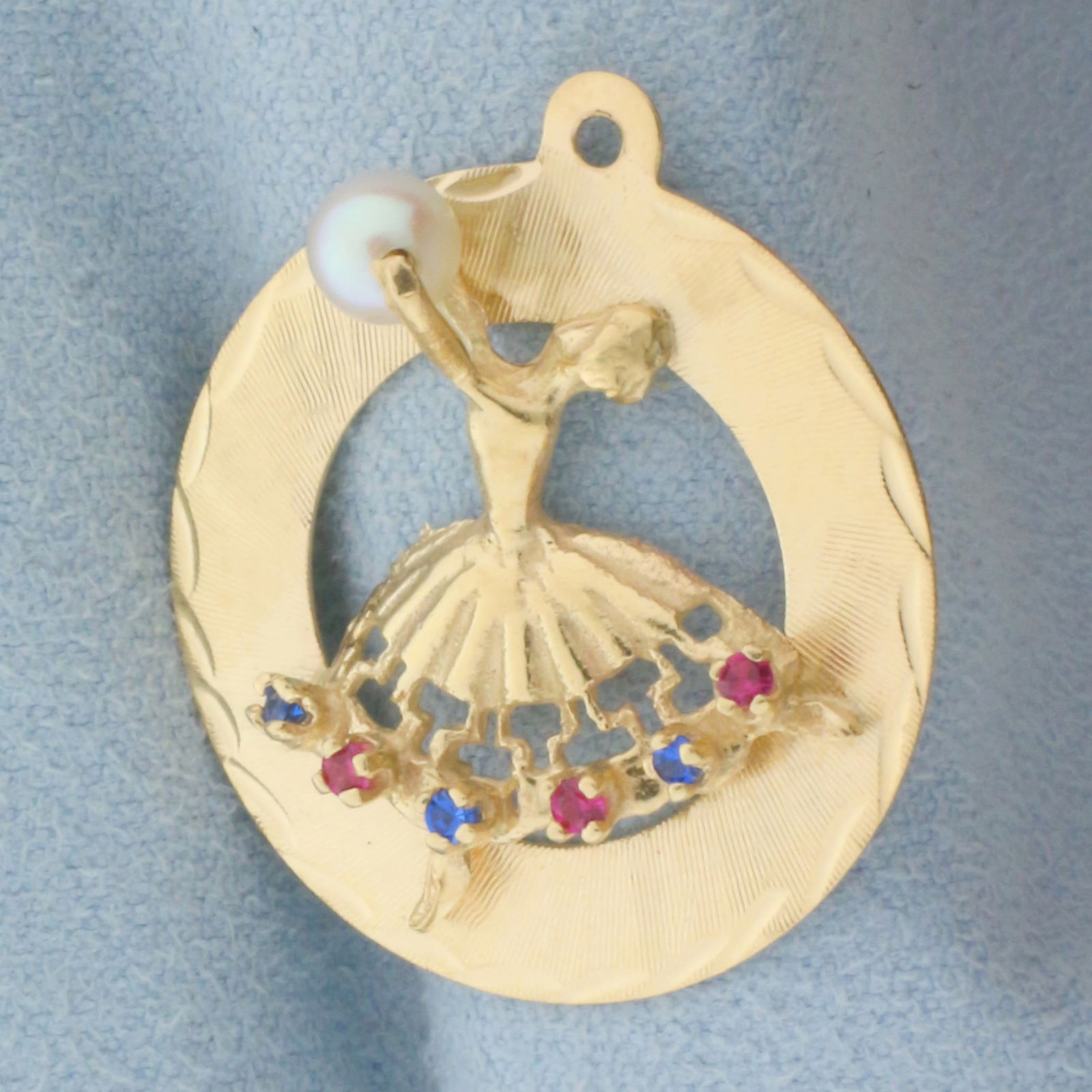 Pearl, Ruby, and Sapphire Dancer Charm or Pendant in 14k Yellow Gold: In 14k Yellow Gold. Contains one high quality 4.5mm cultured pearl with high luster. Pearl spins within dancer's outstretched arms. Also contains three high quality 1.5mm sapphire and ruby gemstones w