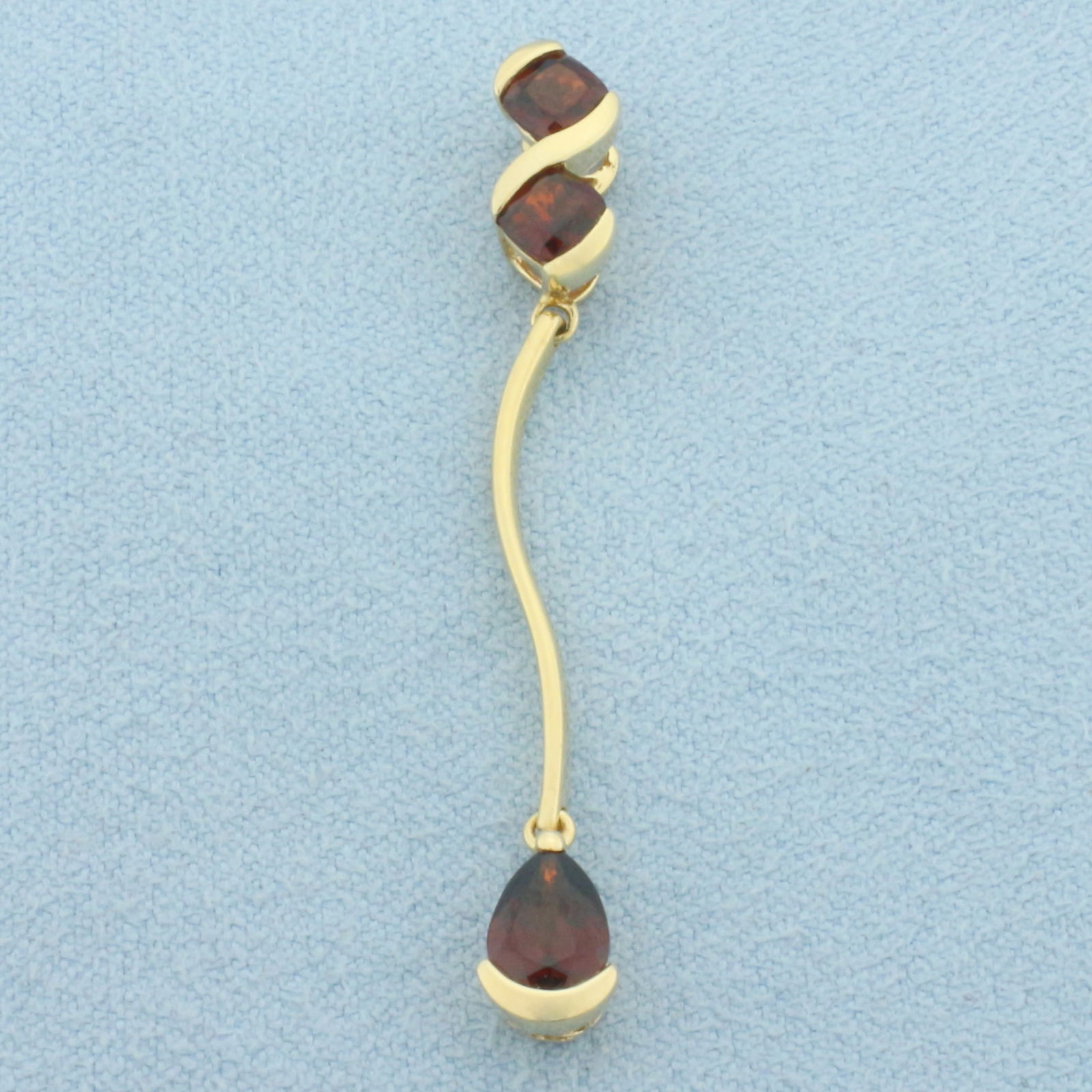Garnet Dangle Pendant in 14k Yellow Gold: In 14k Yellow Gold. Contains one 7mm pear and two 4mm cushion high quality natural Garnet gemstones with intense color and excellent clarity. 1.75 inches long. 1/4 inch wide. 1.9g.