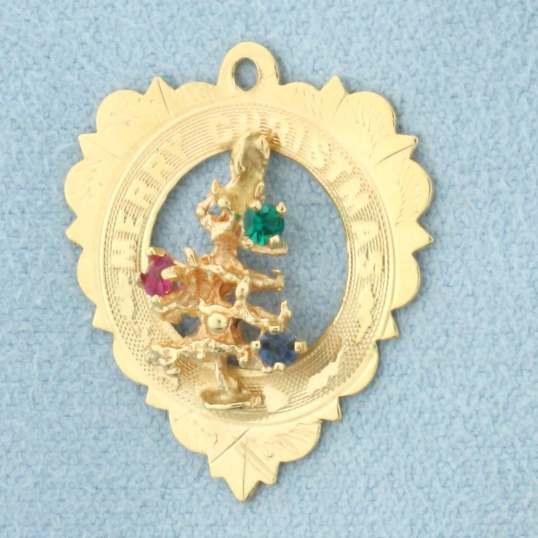 Merry Christmas Heart Charm in 14k Yellow Gold: In 14k Yellow Gold. Contains2mm high quality natural Ruby, Emerald, and Sapphire gemstones with vibrant color. 1 inch long. 3/4 inch wide. 1.6g.
