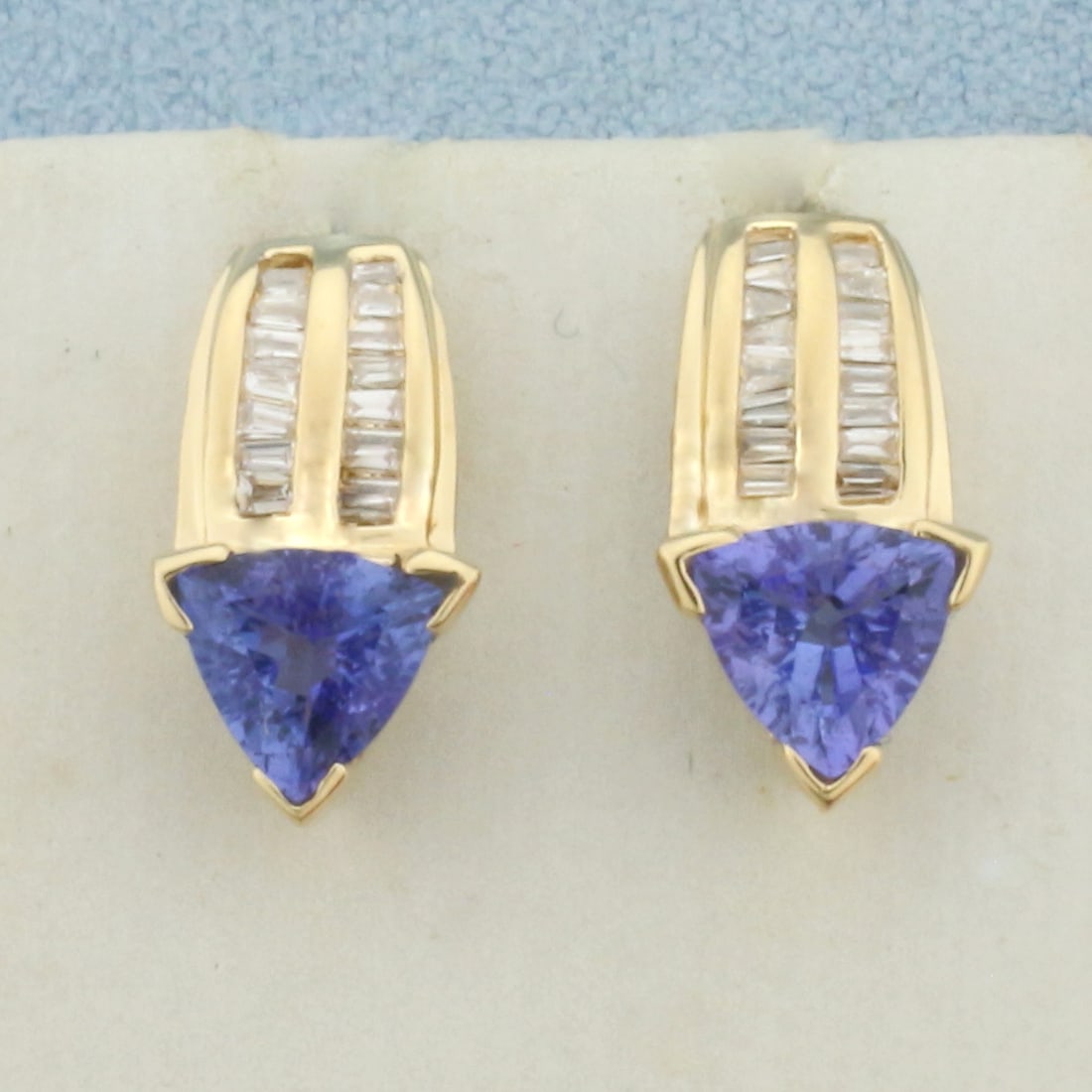 AAA Tanzanite and Diamond Earrings in 14k Yellow Gold: In 14k Yellow Gold. Contains two 6.5mm AAA quality trillion cut natural Tanzanite gemstones, approximately 1.25ct TW, with vibrant color and excellent clarity. Also contains thirty-two high quality 1.