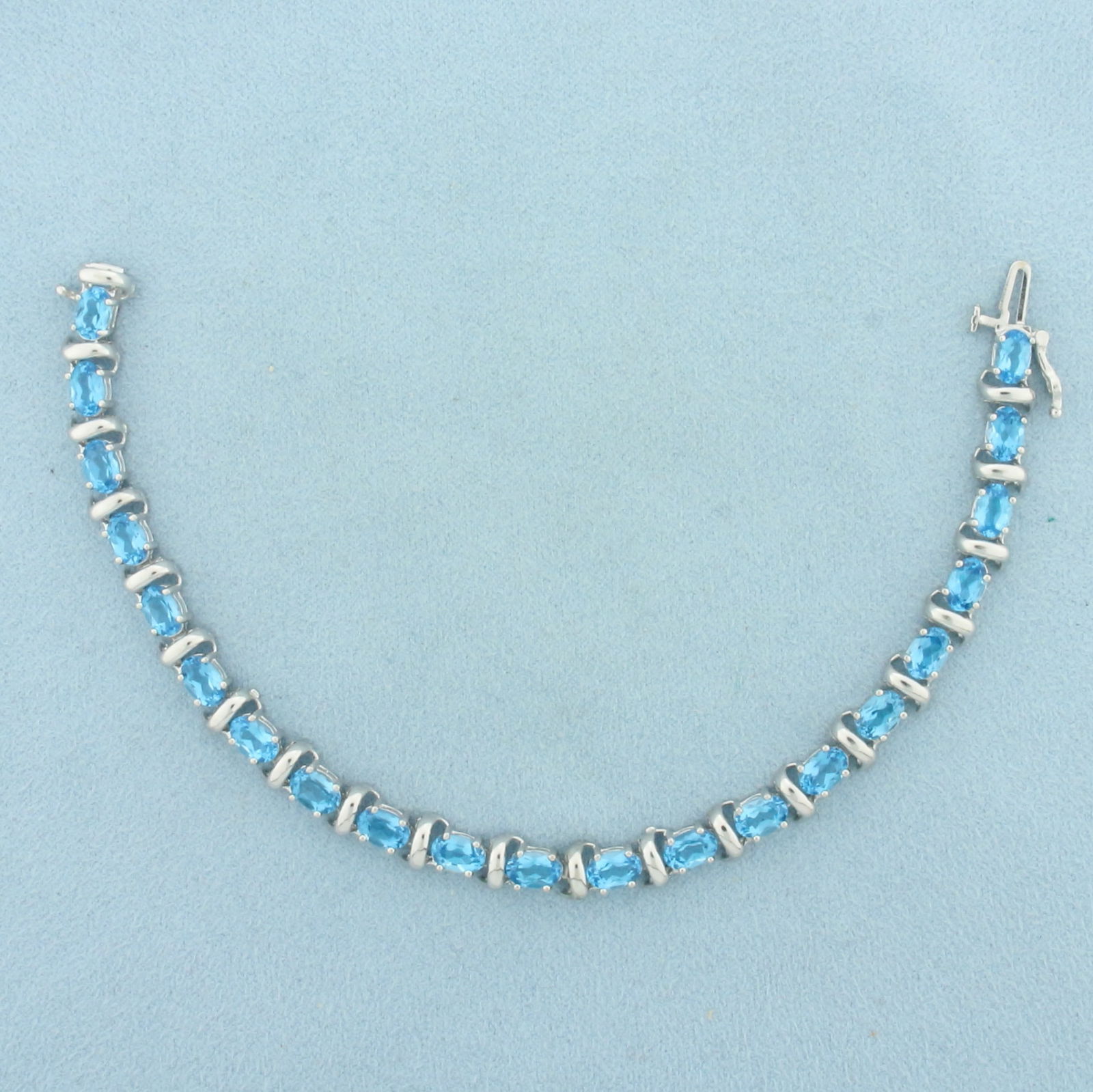 Swiss Blue Topaz Tennis Bracelet in 14k White Gold: In 14k White Gold. Contains twenty-one 4x6mm high quality oval cut natural Blue Topaz gemstones, approximately 10ct TW, with electric blue color and excellent clarity. 7 inches long. 6mm wide. Slide c